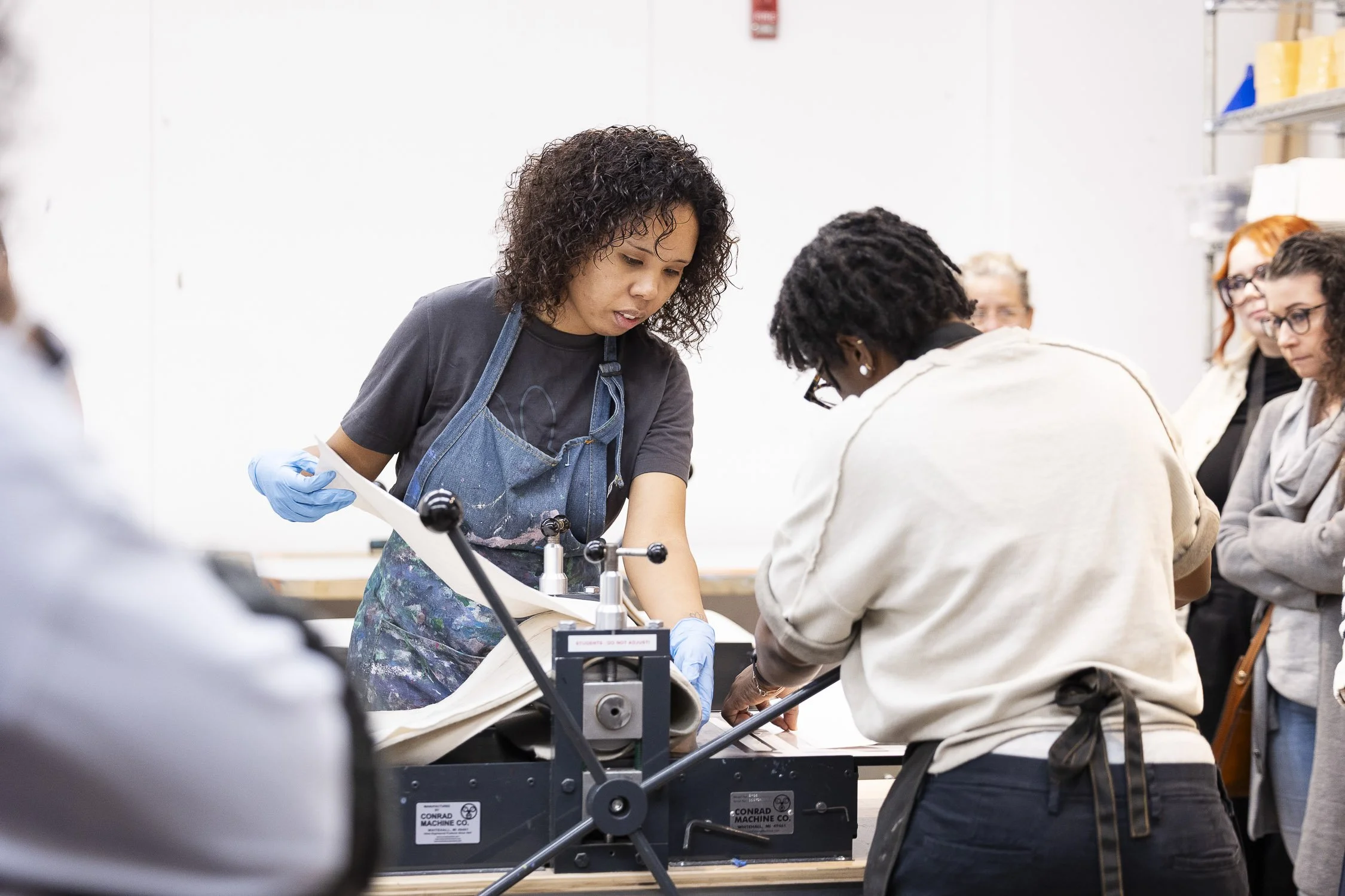 A group of people observing a printing process using a machine in a workshop setting.