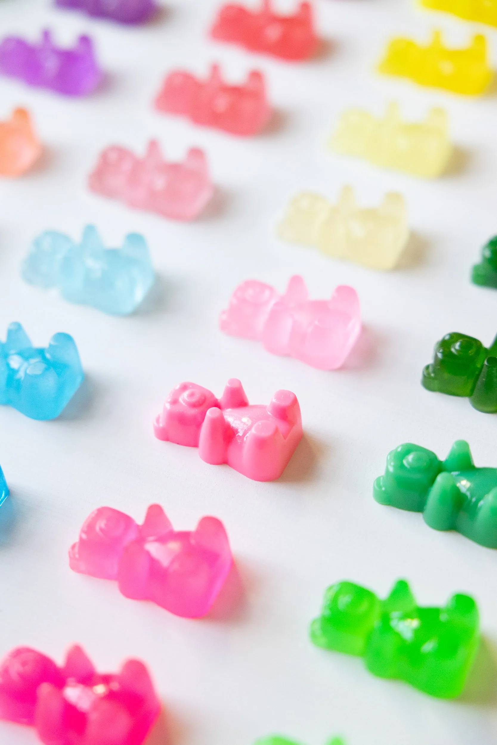 Colorful resin gummy bear-shaped scattered on a white surface.