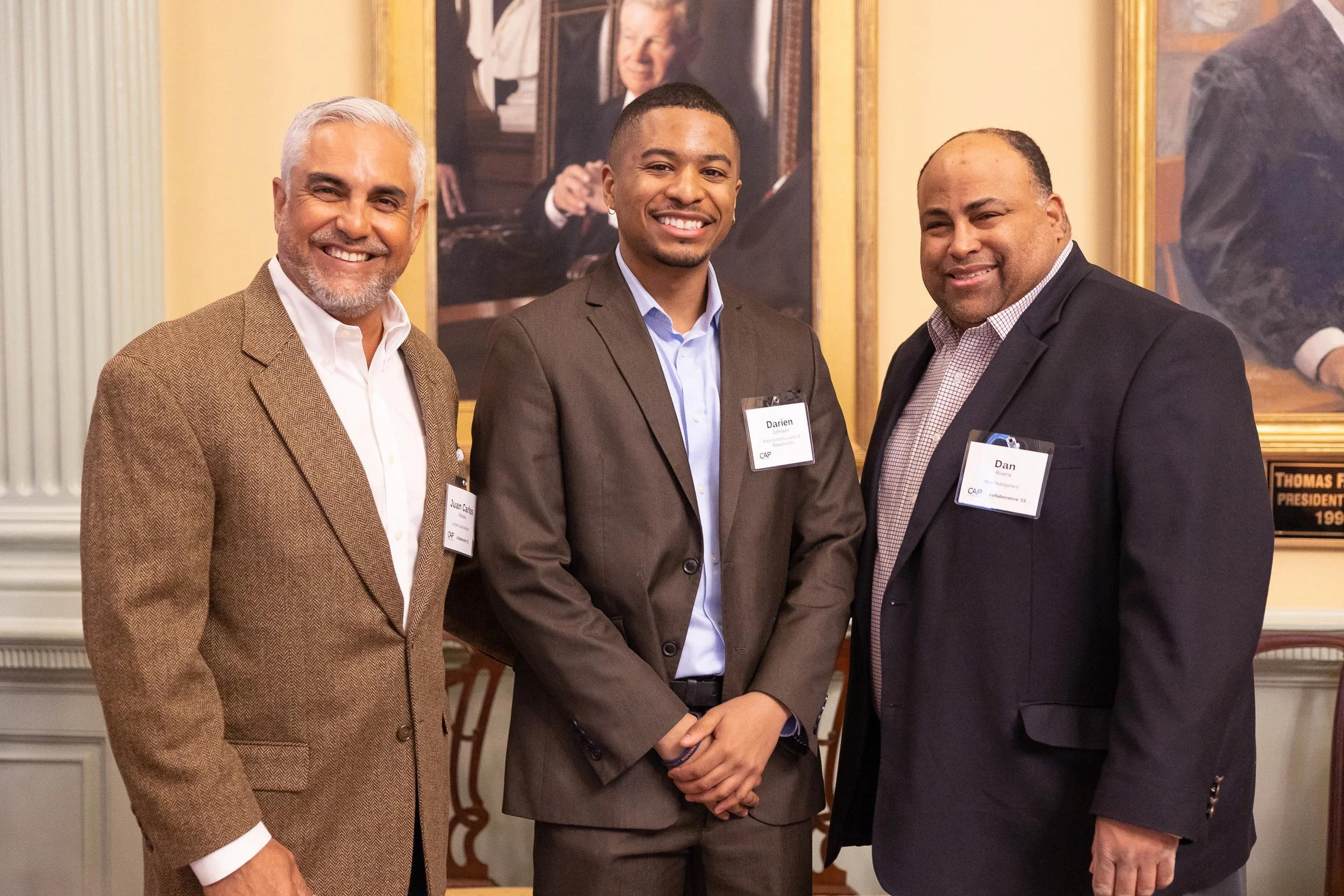Three men in formal attire standing together at event at the Massachusetts State House in Boston.