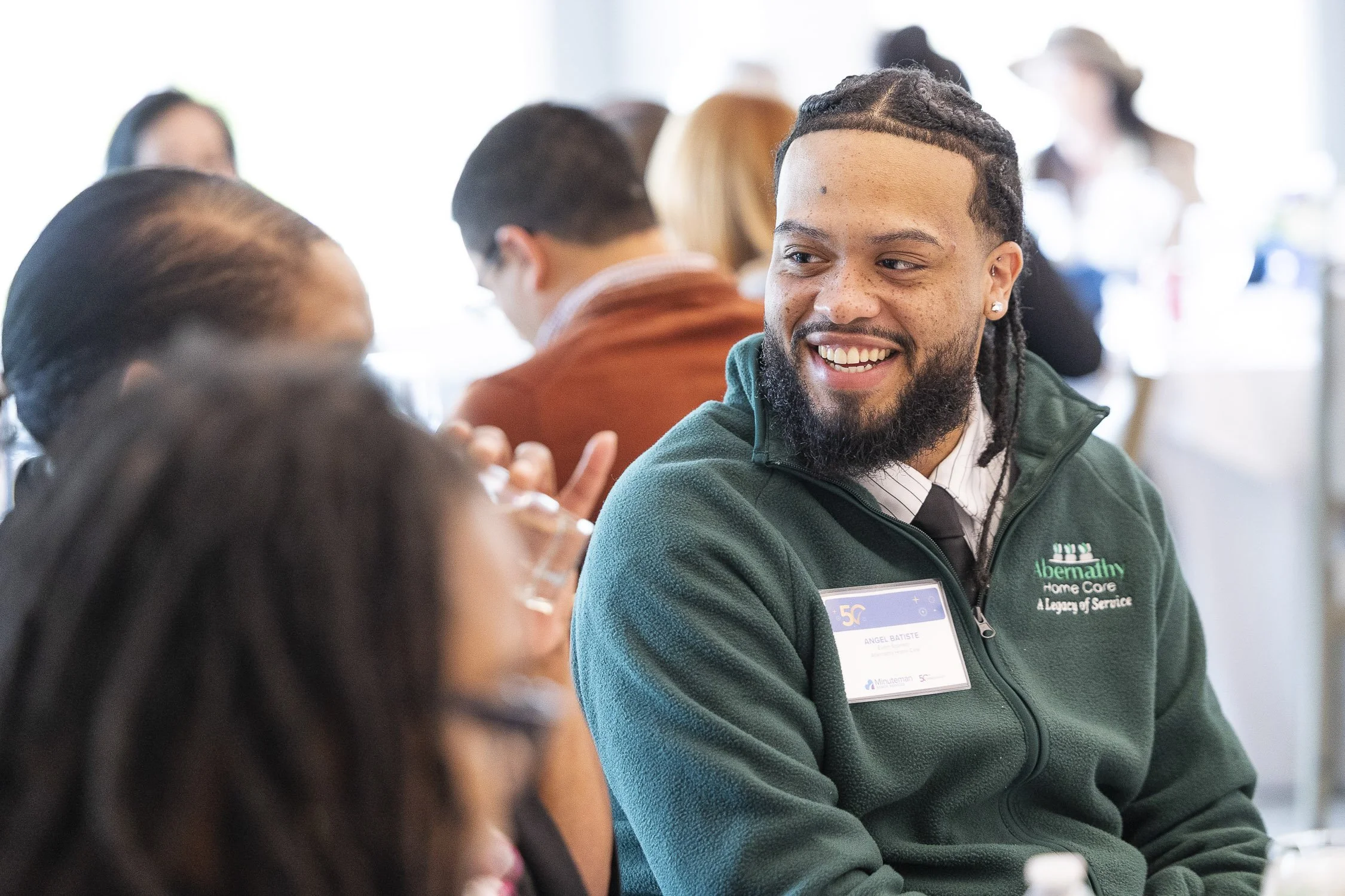 A smiling man sitting at a table in a lively indoor setting during a nonprofit event in Boston, Massachusetts.