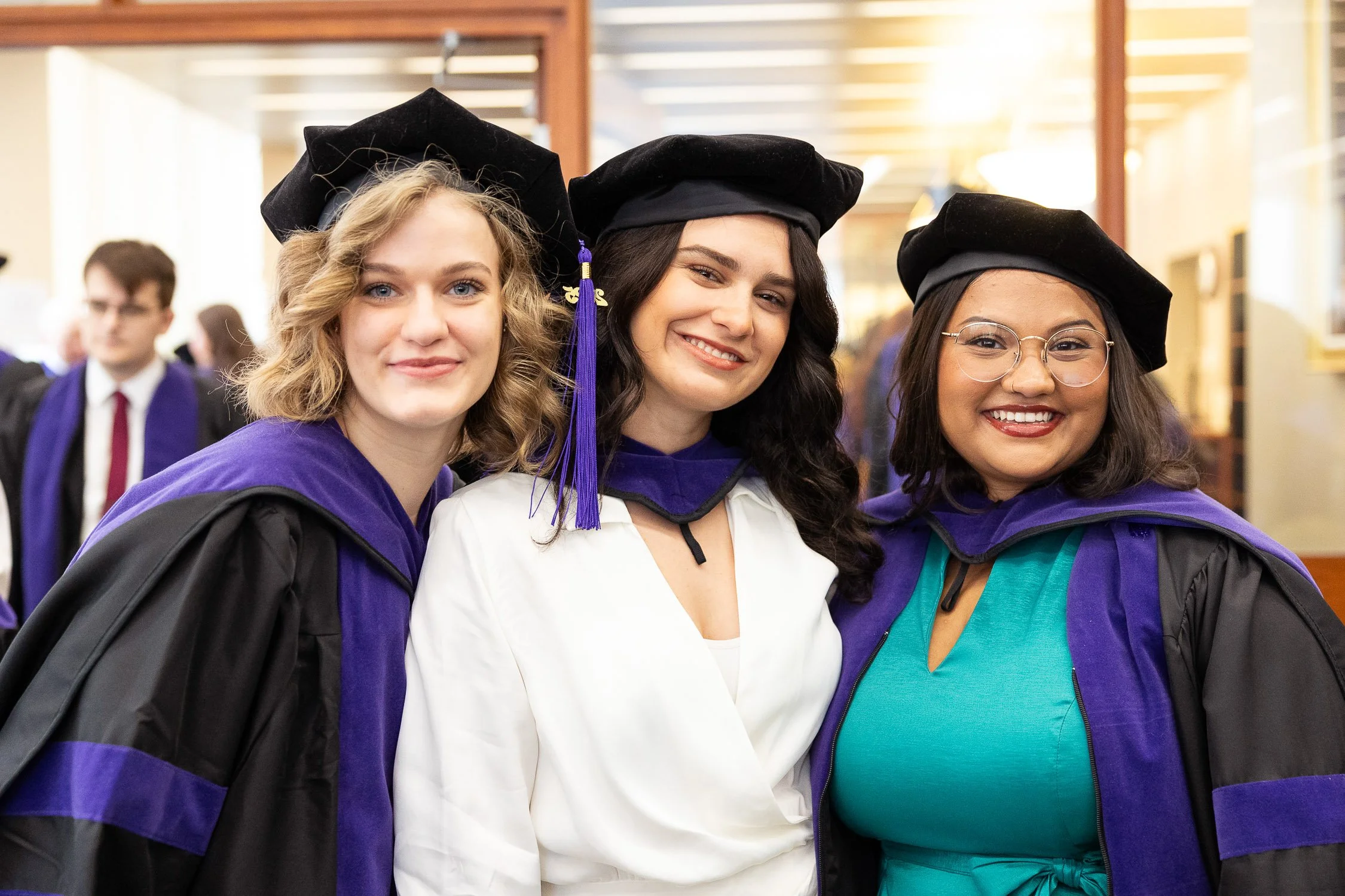 Three women in graduation caps and gowns smiling before the ceremony in Boston.