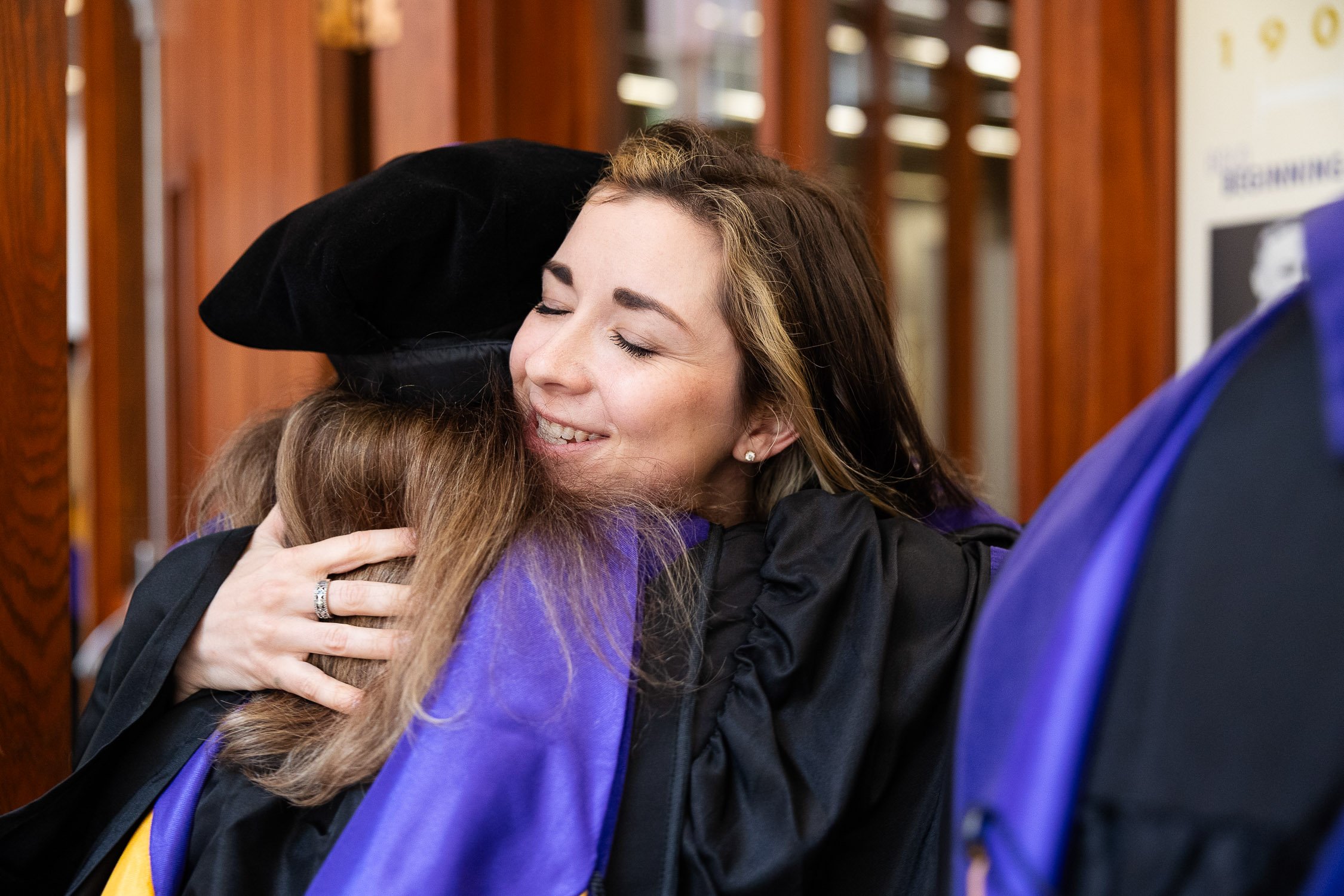 A woman in graduation attire hugging someone at New England Law Boston.