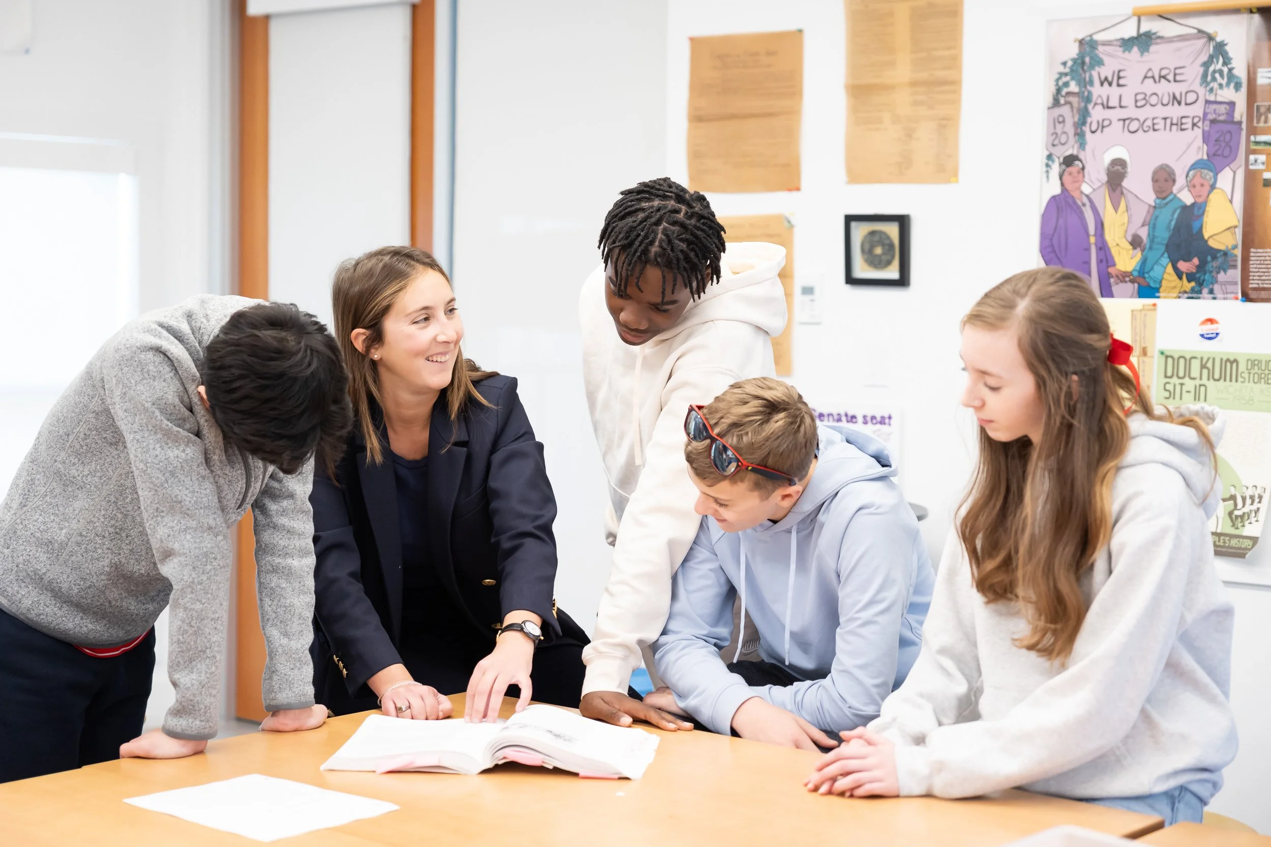 A group of five young students and a teacher gathered around an open book on the table at a private school in Dover, Massachusetts.