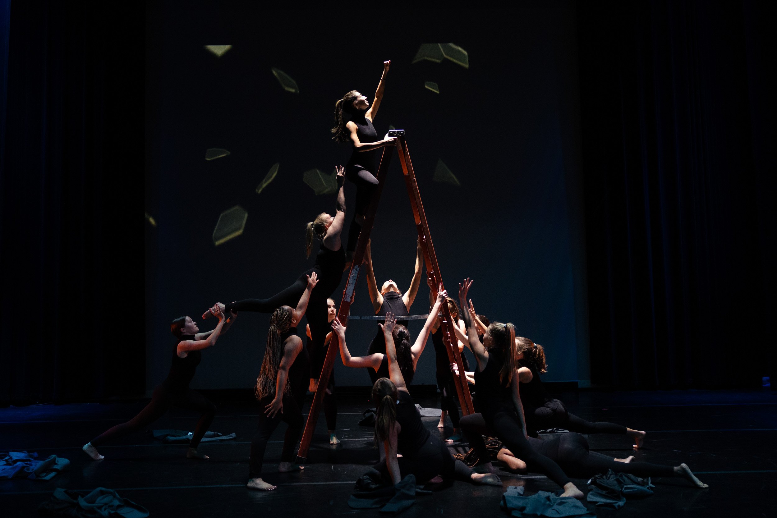A group of performers forming a human pyramid on stage, with one person standing on top, at a private school dance performance in Newton, Massachusetts.