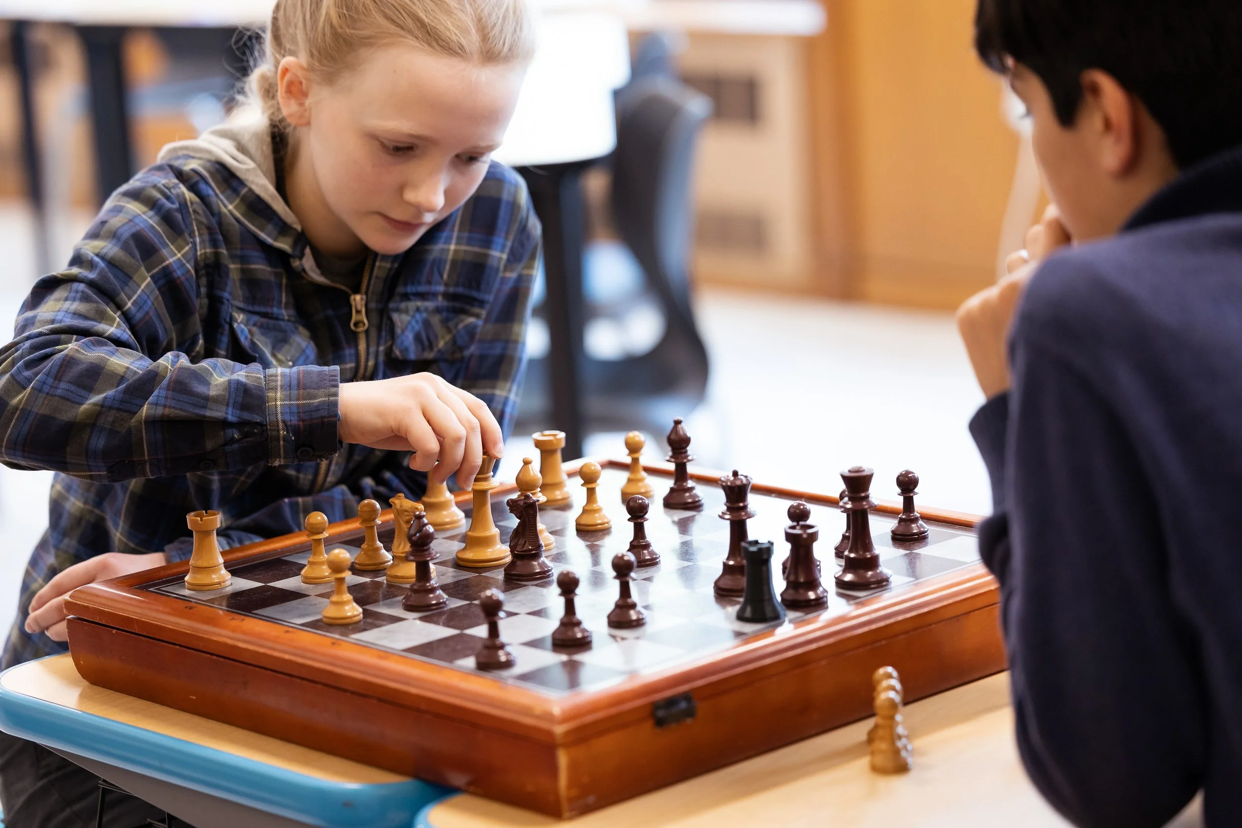 Two middle school students playing chess at a table at a Massachusetts Montessori school.