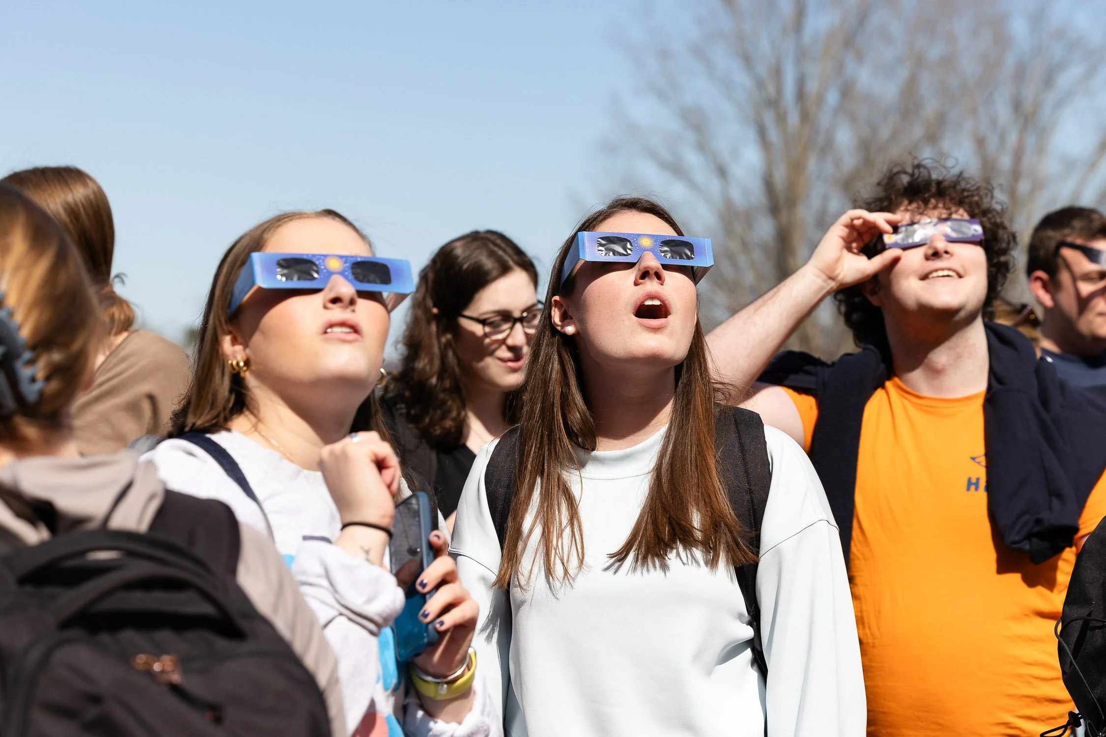 Group of Saint Anselm College students wearing solar eclipse glasses, looking up at the sky.