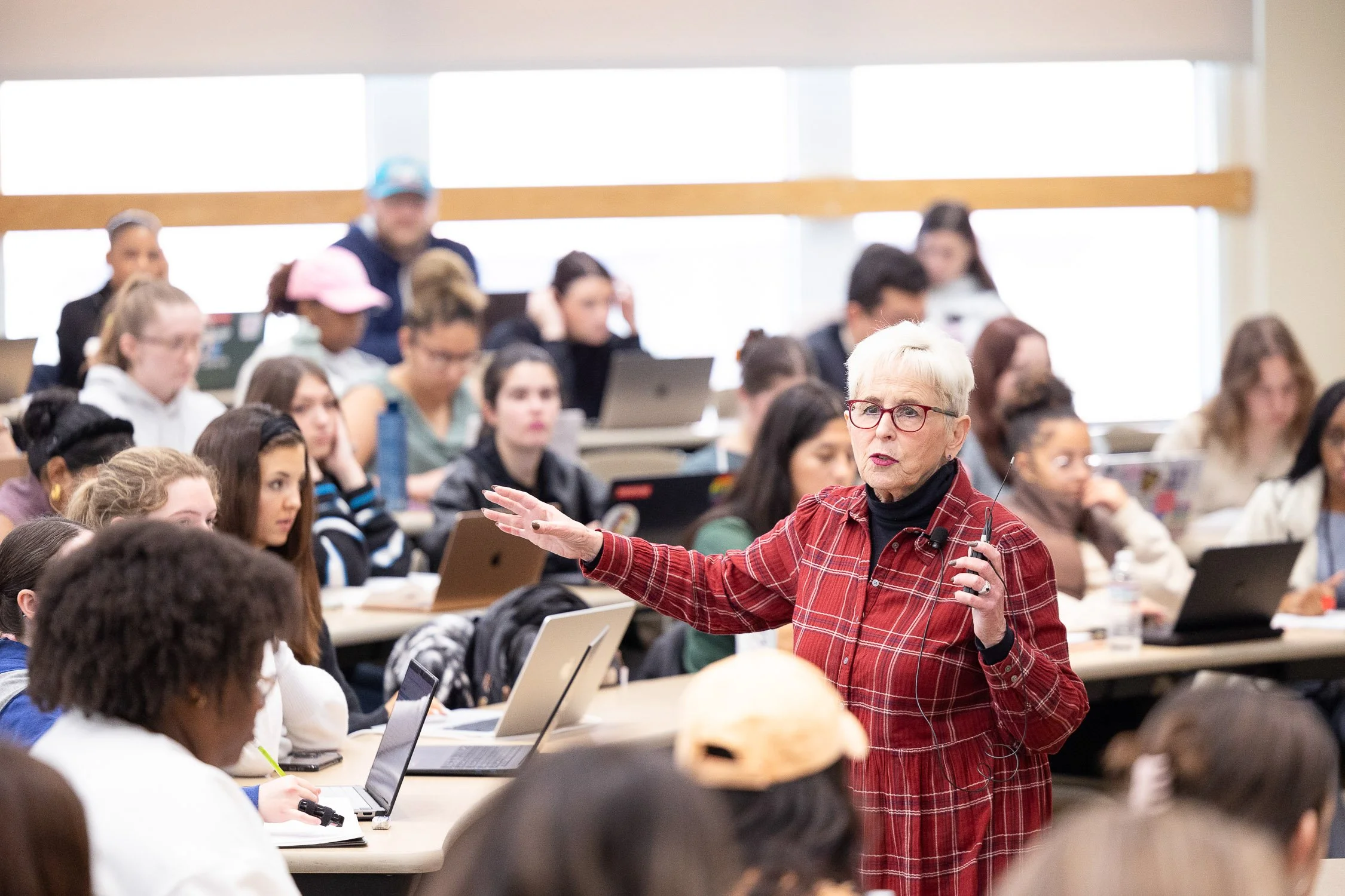 A lecture hall full of students sitting at desks with laptops, listening to a female law professor at a law school in Boston.