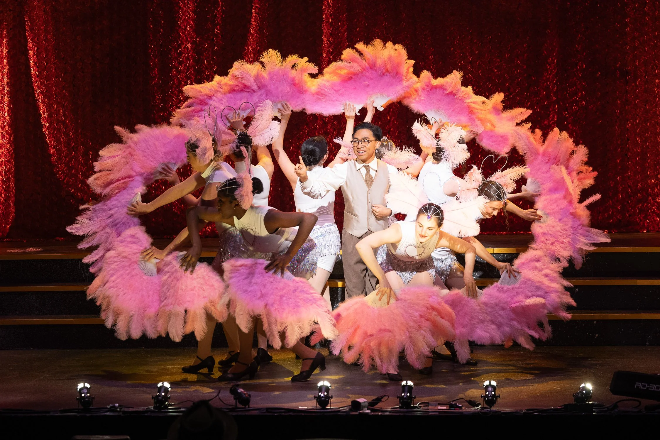 Theatrical stage performance with of Chicago with dancers in pink feather costumes.