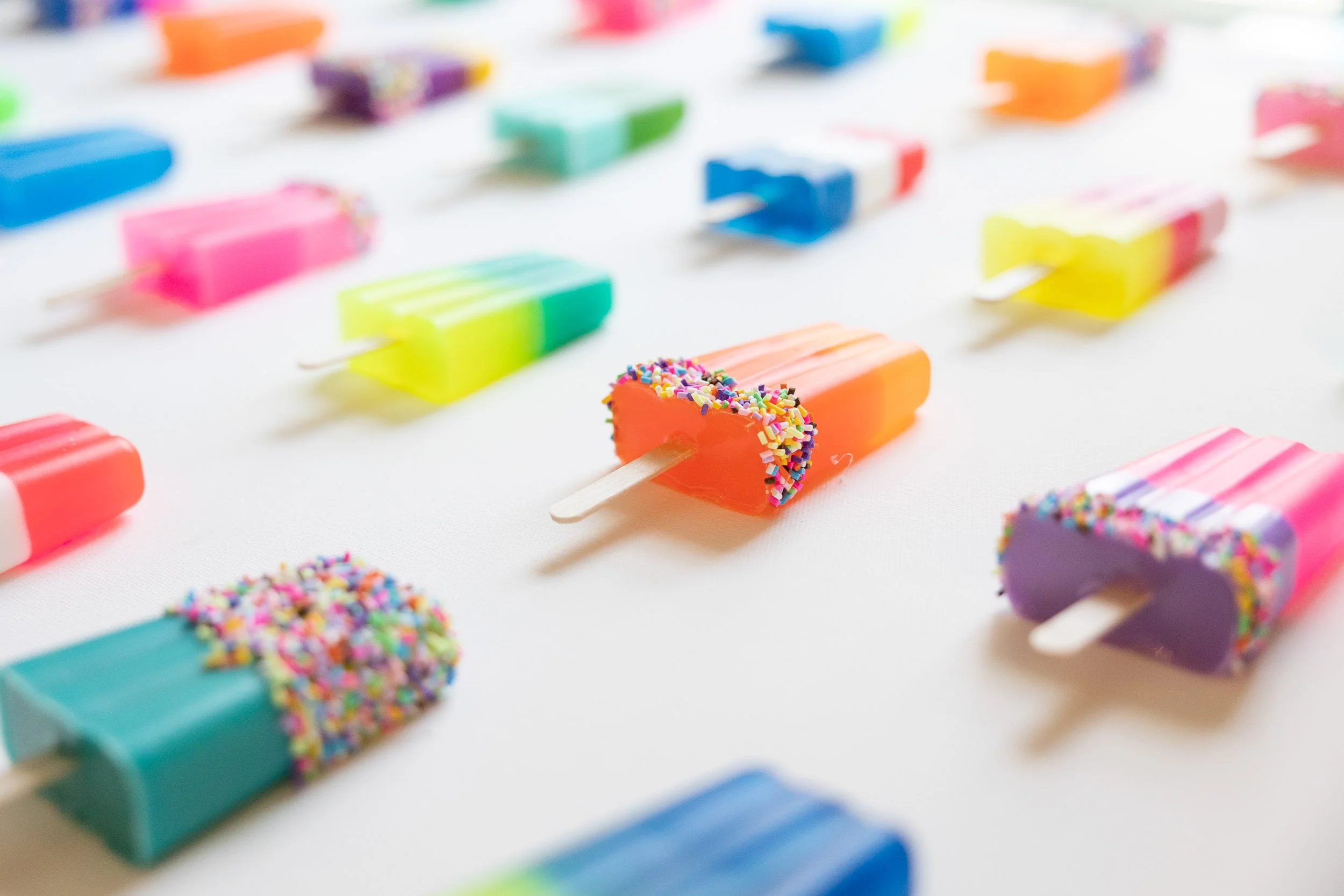 Colorful resin popsicles with sprinkles on a white background.