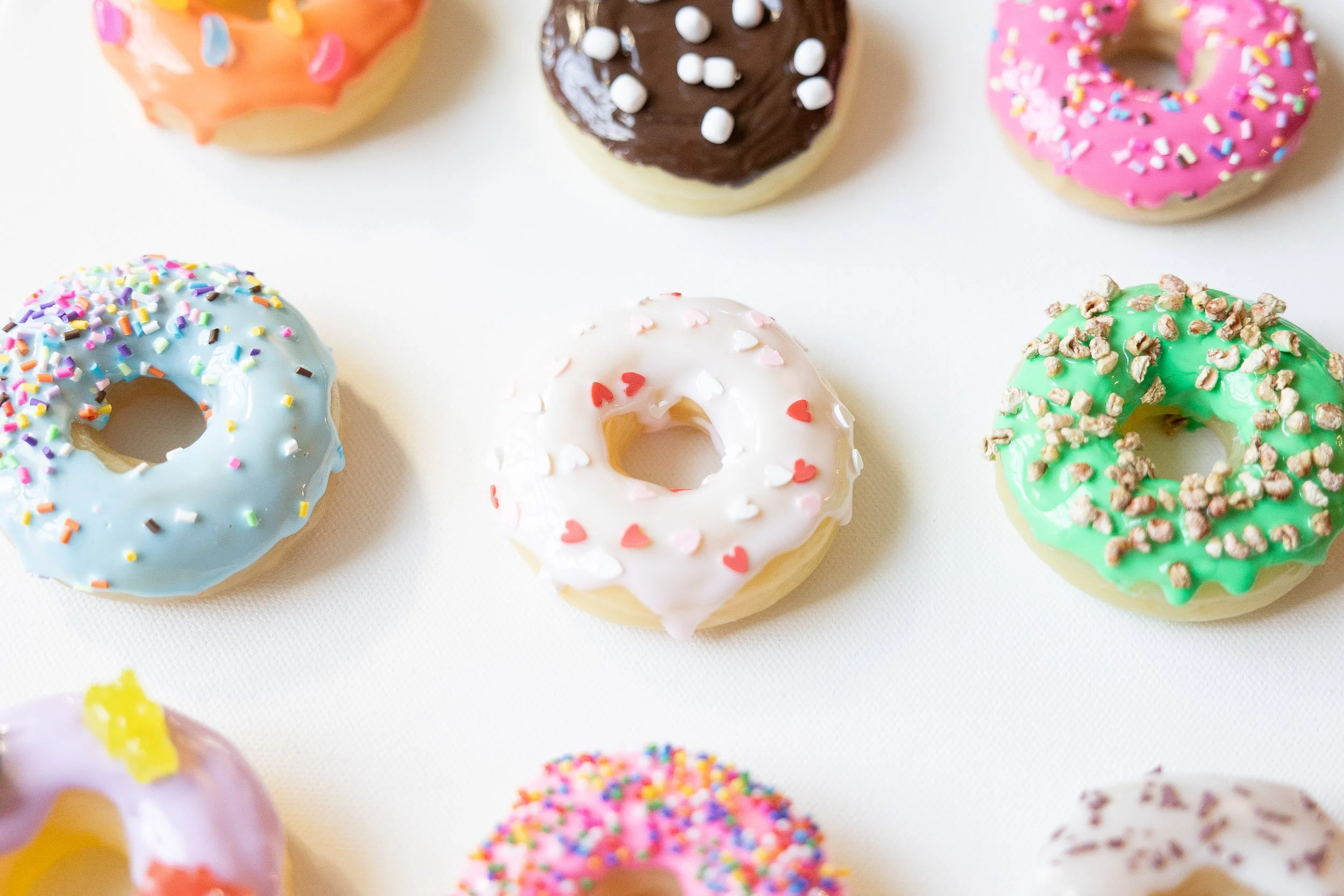 Assorted colorful resin donuts with various toppings on a white surface.