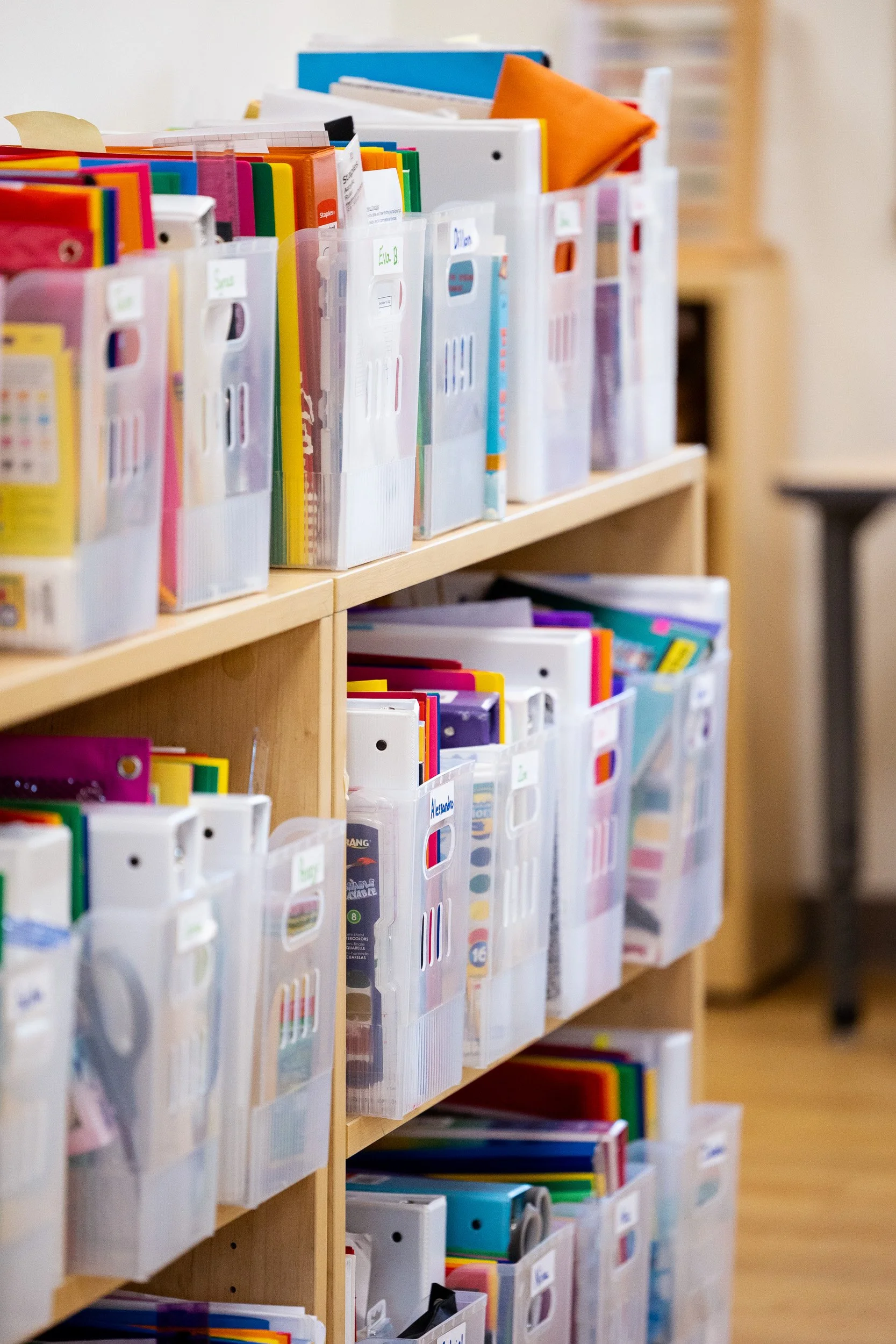 Organized wooden shelves filled colorful folders and notebooks in a Montessori classroom.