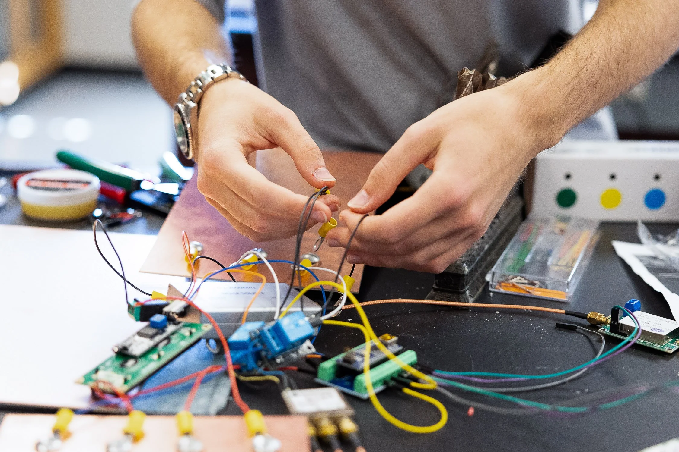 Student working on an electronics project with wires, circuit boards, and tools at a New Hampshire college.