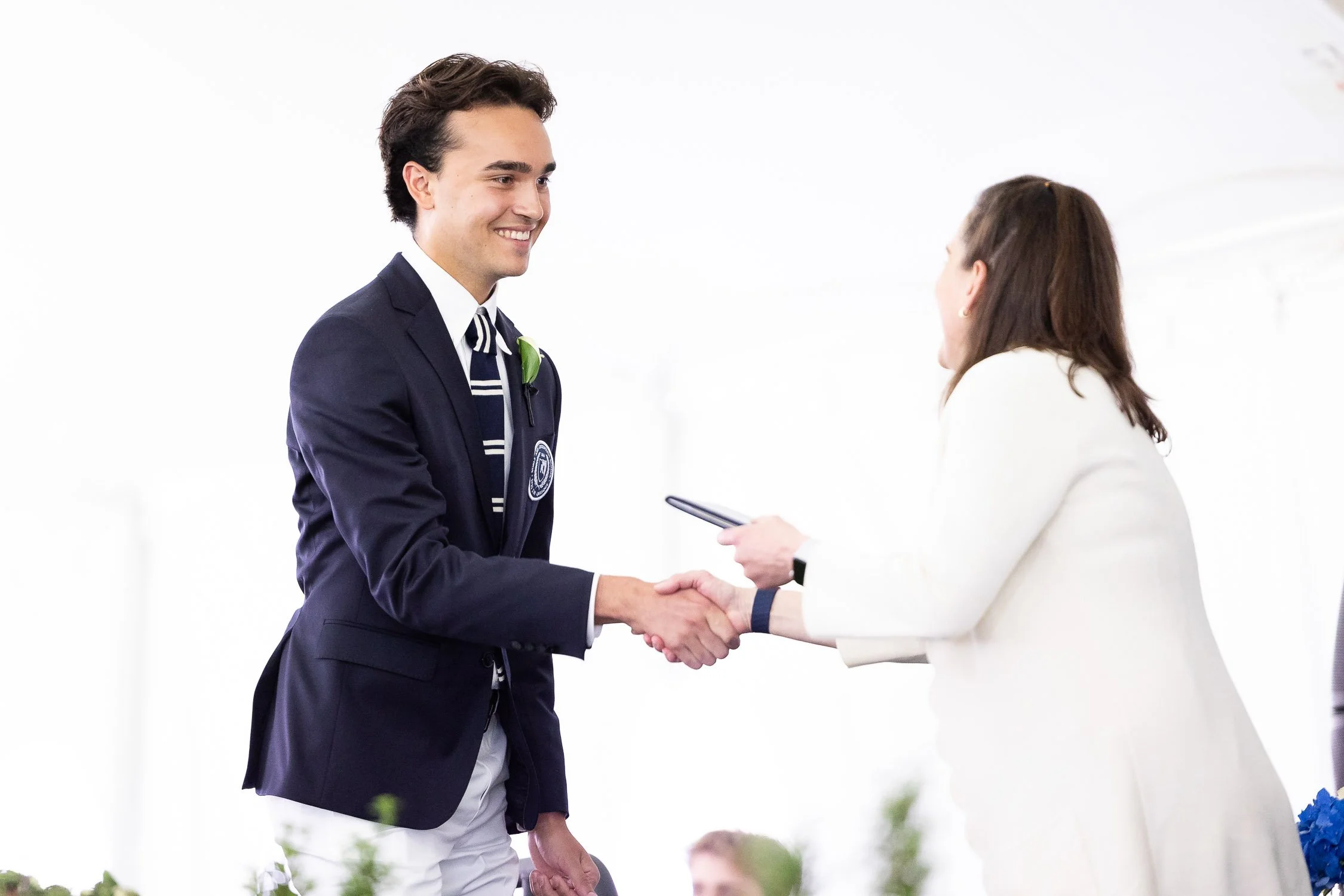 A high school student receiving diploma at graduation ceremony under tent in Boston.