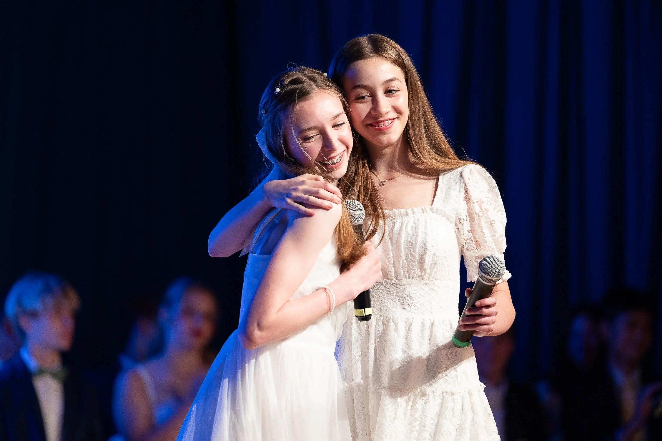 Two middle school girls hugging on stage during a performance at Charles River School graduation.