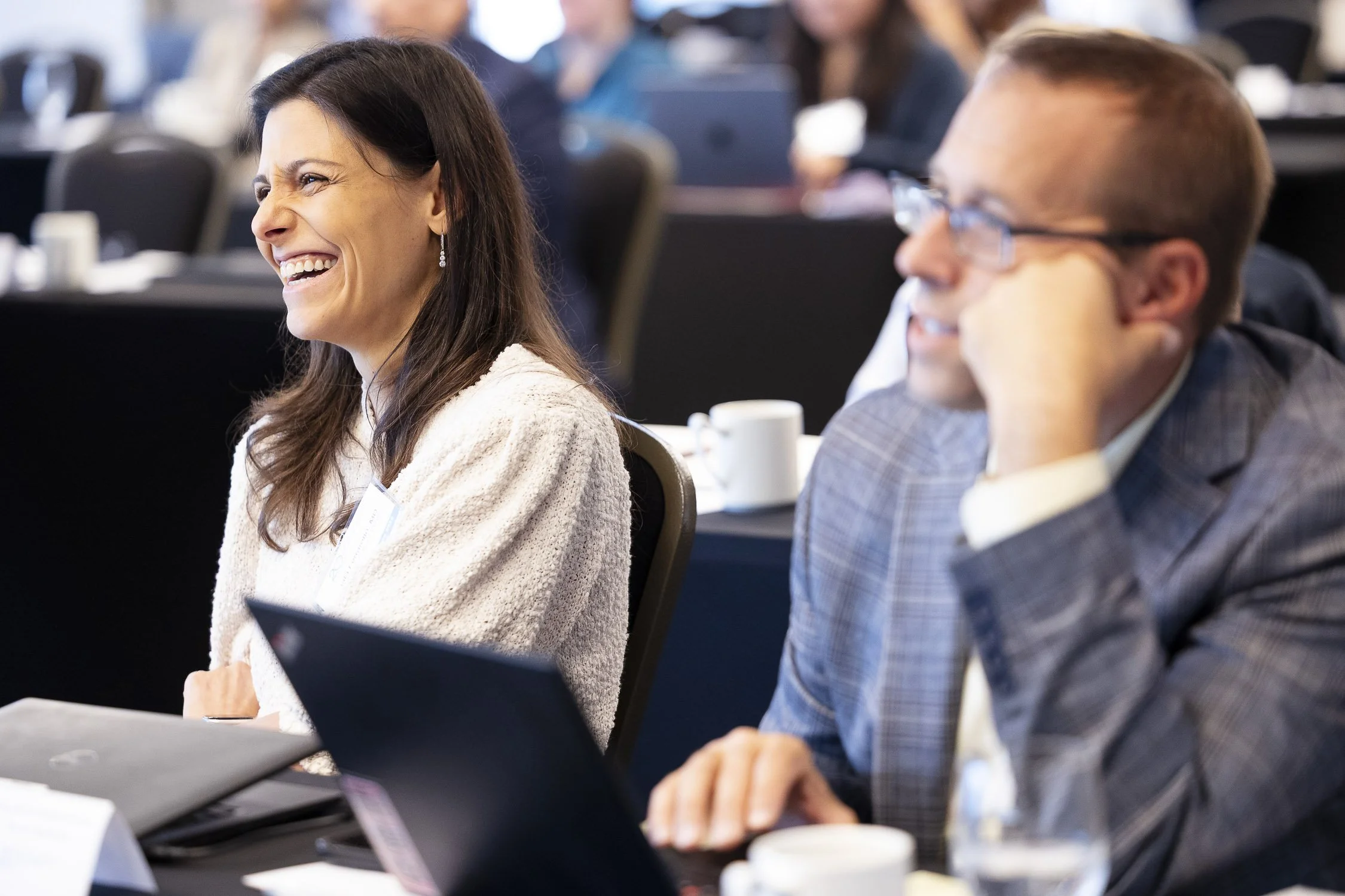 People attending a biotech conference at a hotel in Boston, Massachusetts, sitting at tables with laptops and coffee cups, engaged and smiling