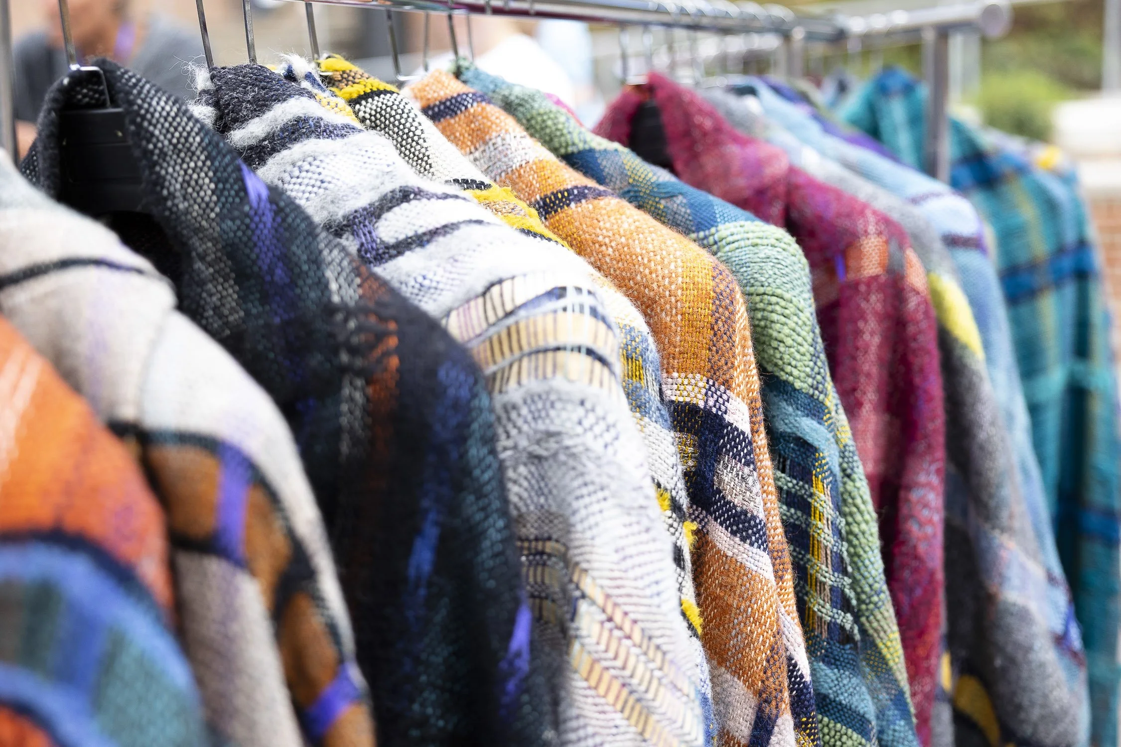 Colorful, patterned sweaters hanging on a rack at an outdoor market at RISD Craft in Providence, Rhode Island.