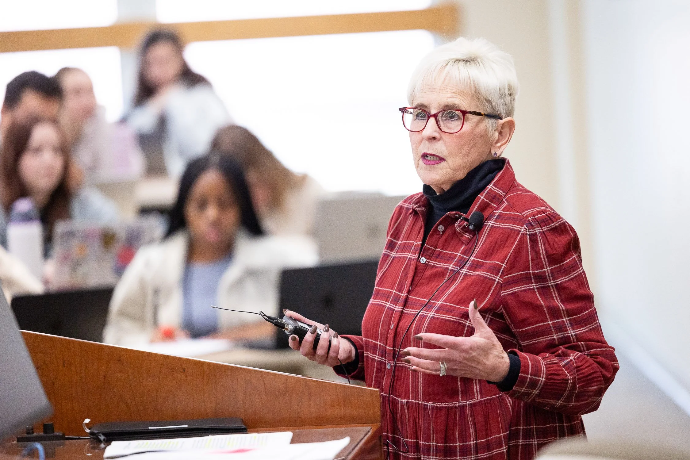 An woman is standing at a podium, speaking to a group of people in a classroom at a New England law school.