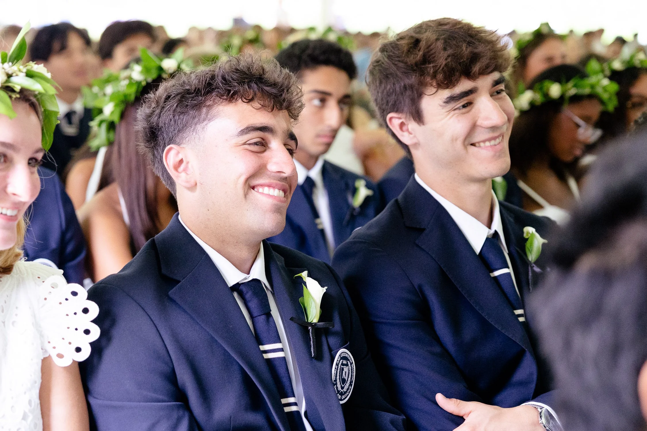 Two young men in navy blue suits laugh at a private school graduation ceremony in Dedham.