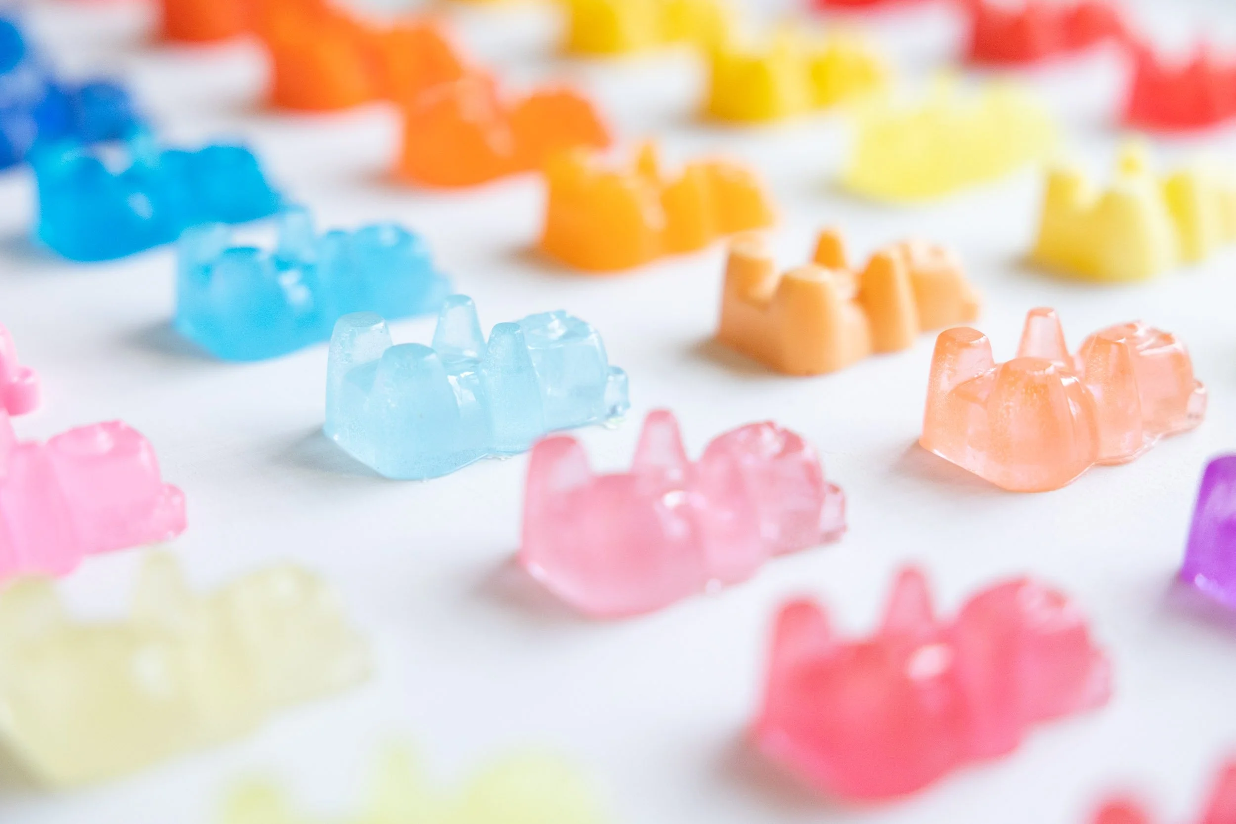 Close-up of colorful resin gummy bears arranged on a white surface.