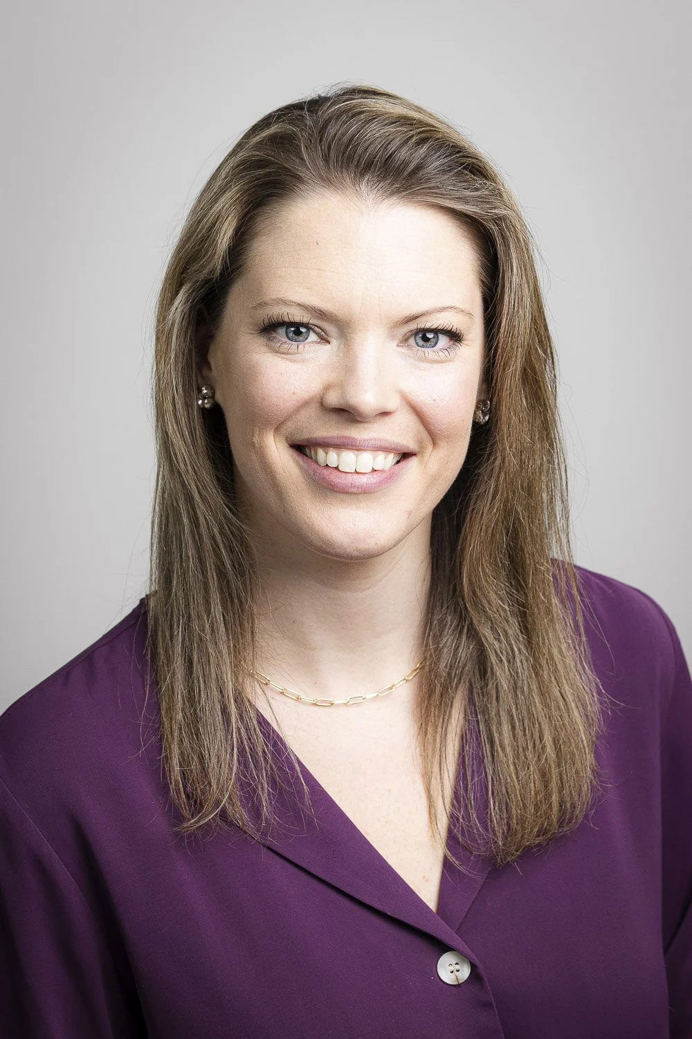 Headshot of a woman with shoulder-length light brown hair, blue eyes, wearing a purple blazer, smiling at the camera.