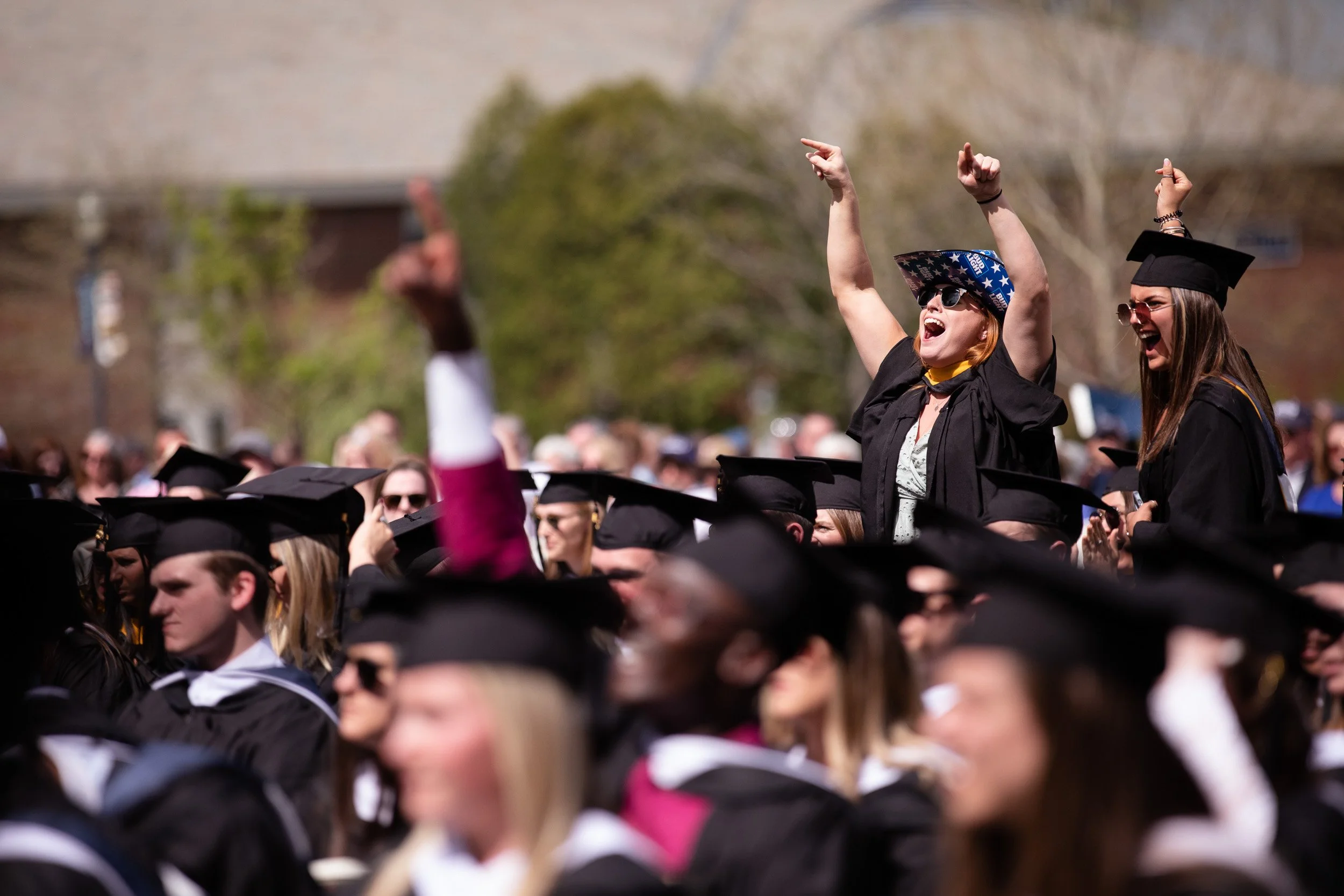 A crowd of graduates in caps and gowns celebrating outdoors on graduation day.