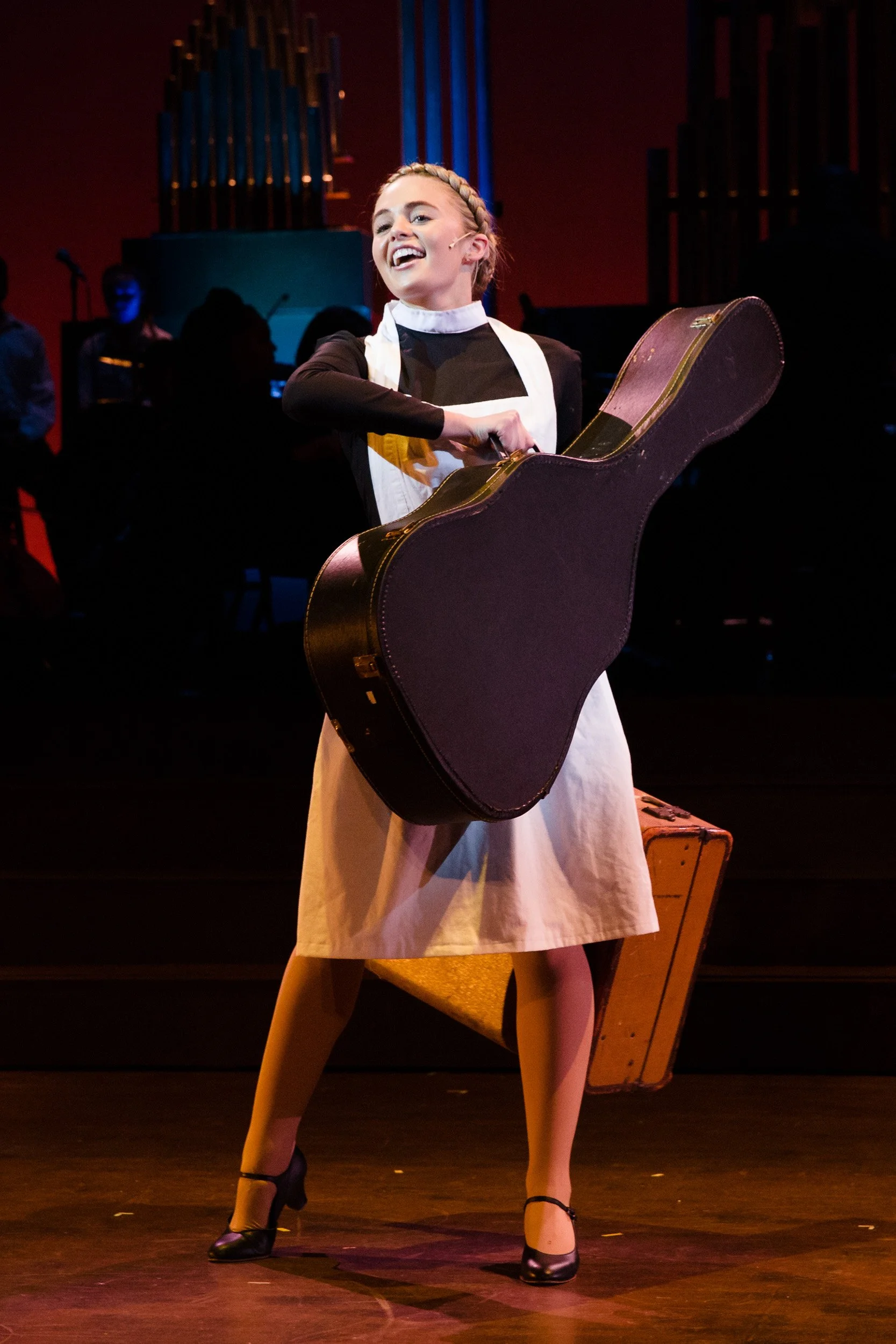 A high school actor performing on stage with a guitar case, in a Massachusetts private school production of The Sound of Music.