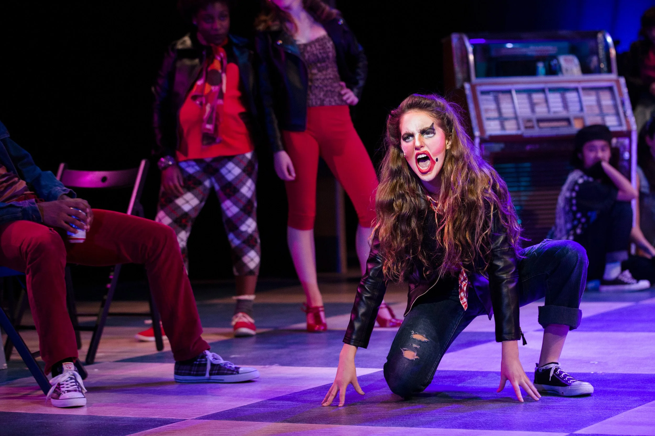 A high school girl wearing a black leather jacket and ripped jeans performs during a musical production at an independent school in Boston, Massachusetts.