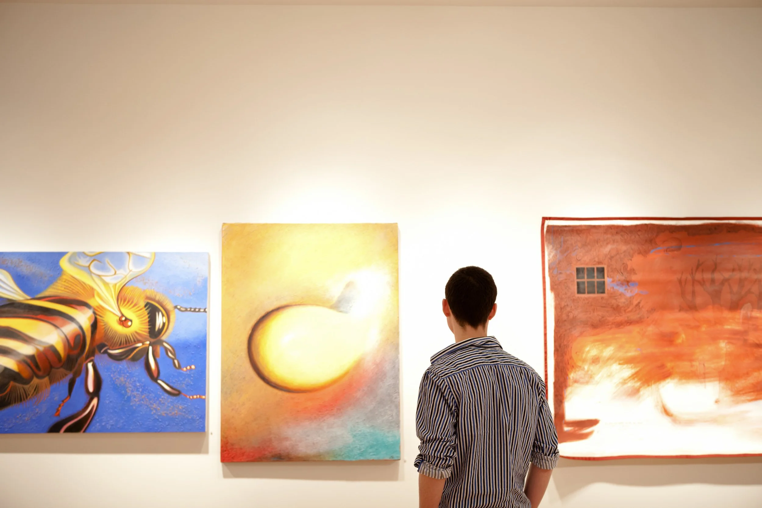 A man viewing colorful paintings in an art gallery.