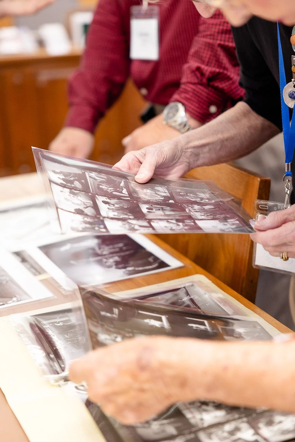 People reviewing black and white photo contact sheets on a table.