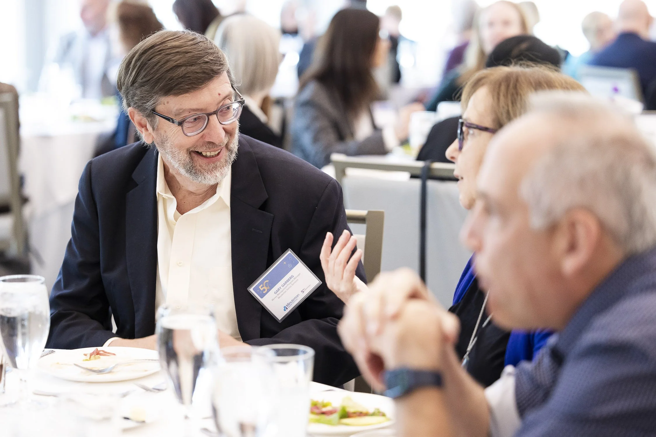 A man with glasses and a beard smiling and talking to a woman during a nonprofit event in Boston, Massachusetts.