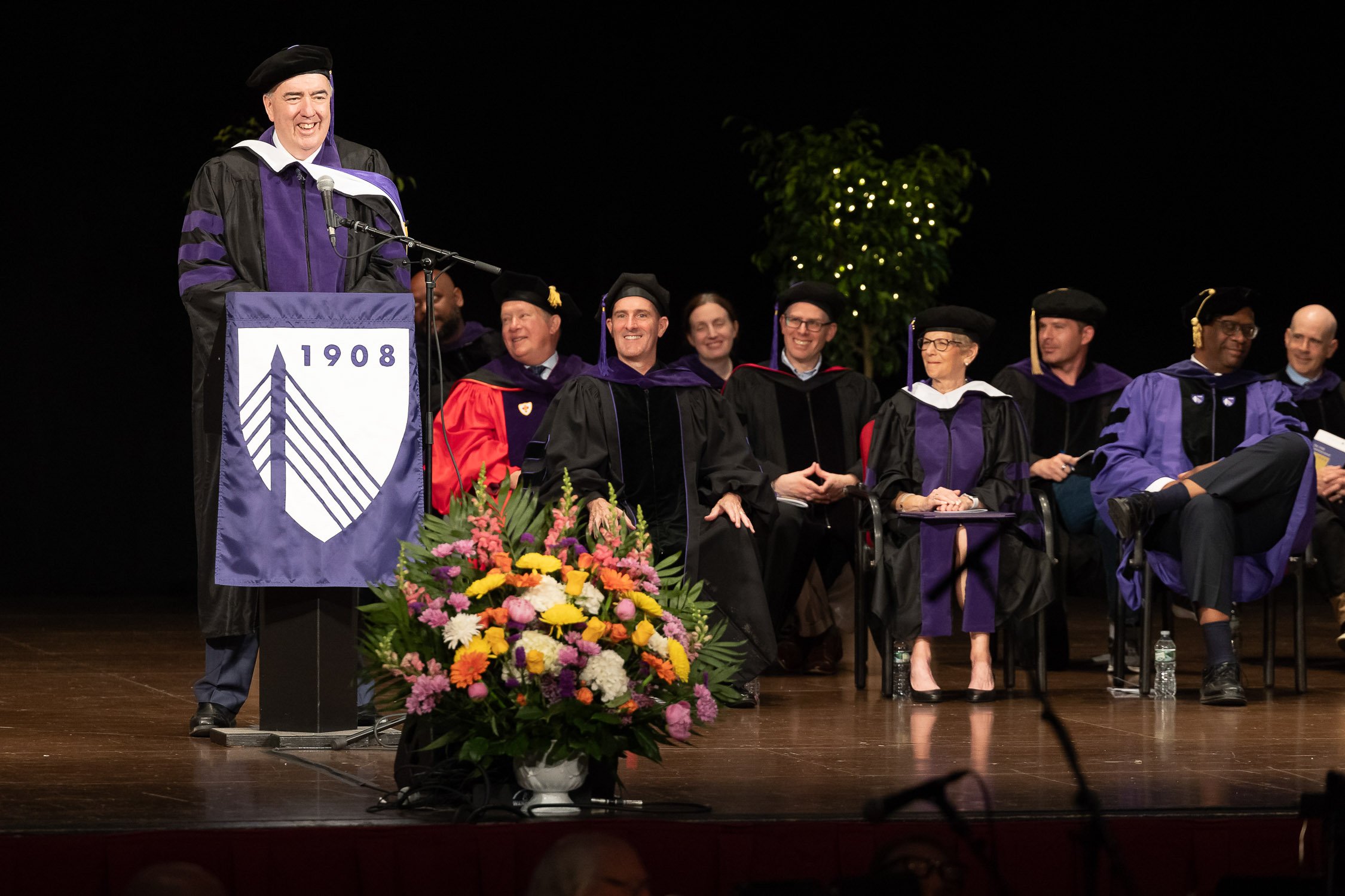 A graduation ceremony on stage with a speaker at the podium at the Wang Theater in Boston.