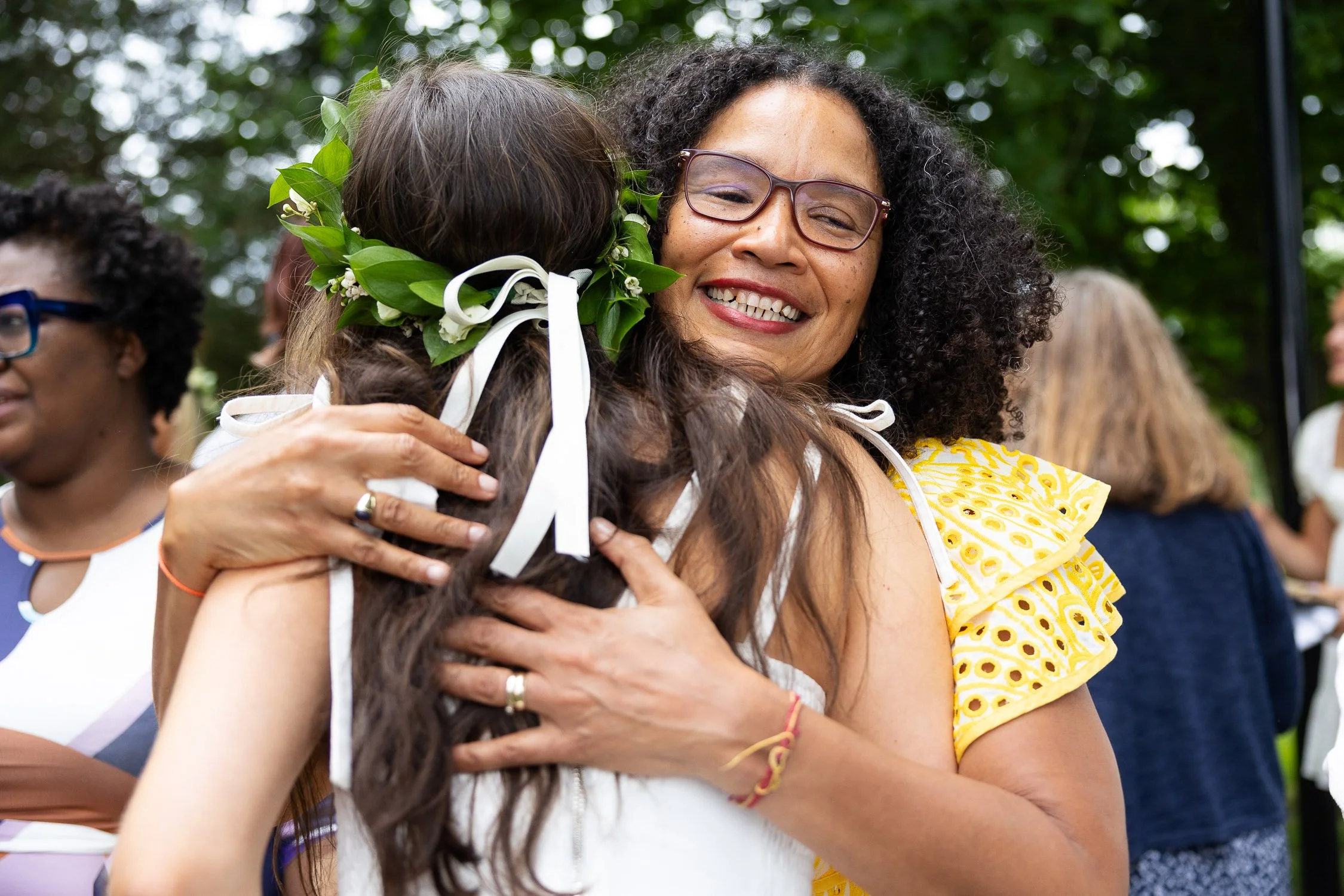 A woman hugging a girl with a floral crown after an outdoor graduation celebration.