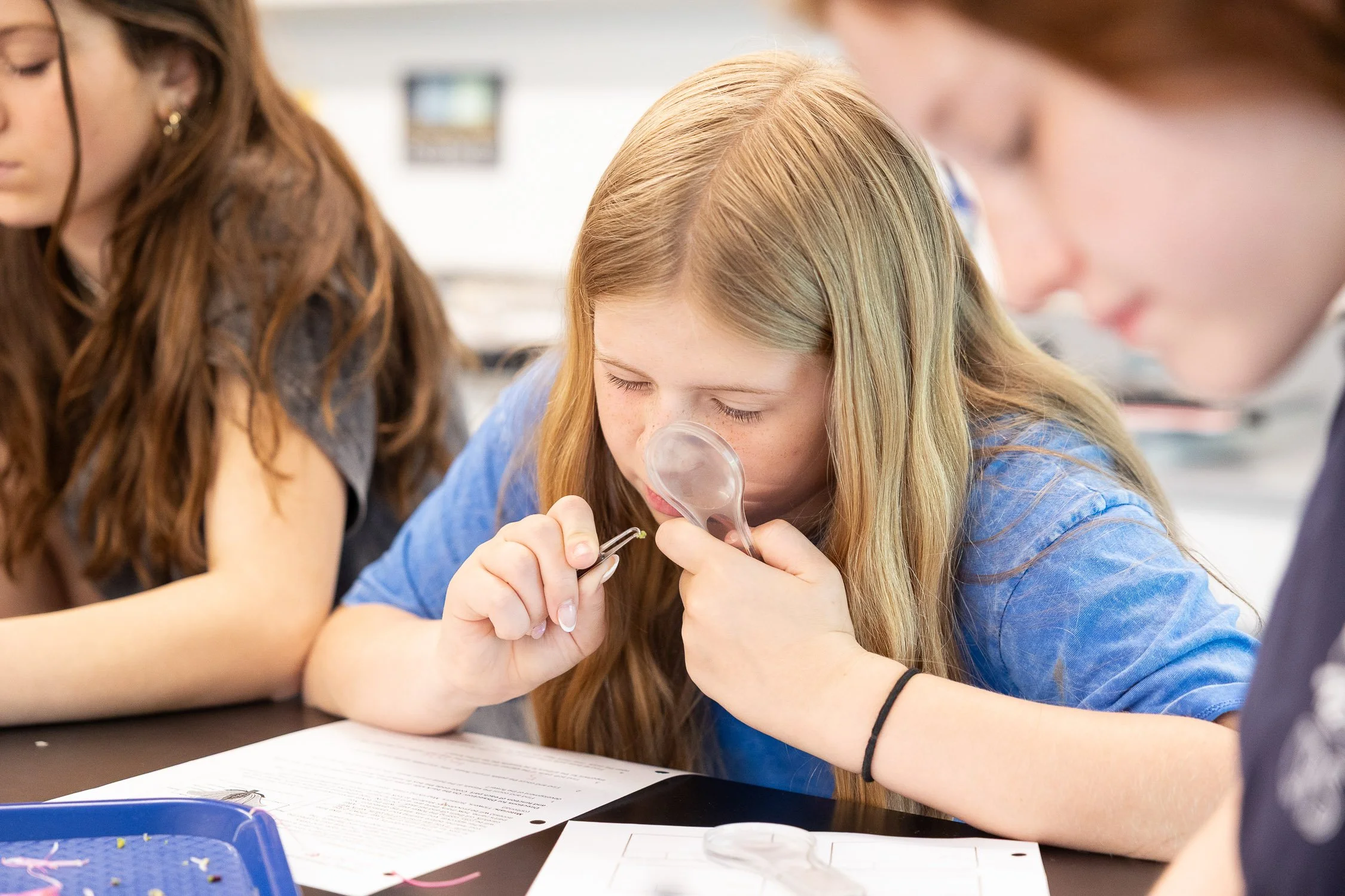 Girl examining a sample with a magnifying glass in a classroom setting