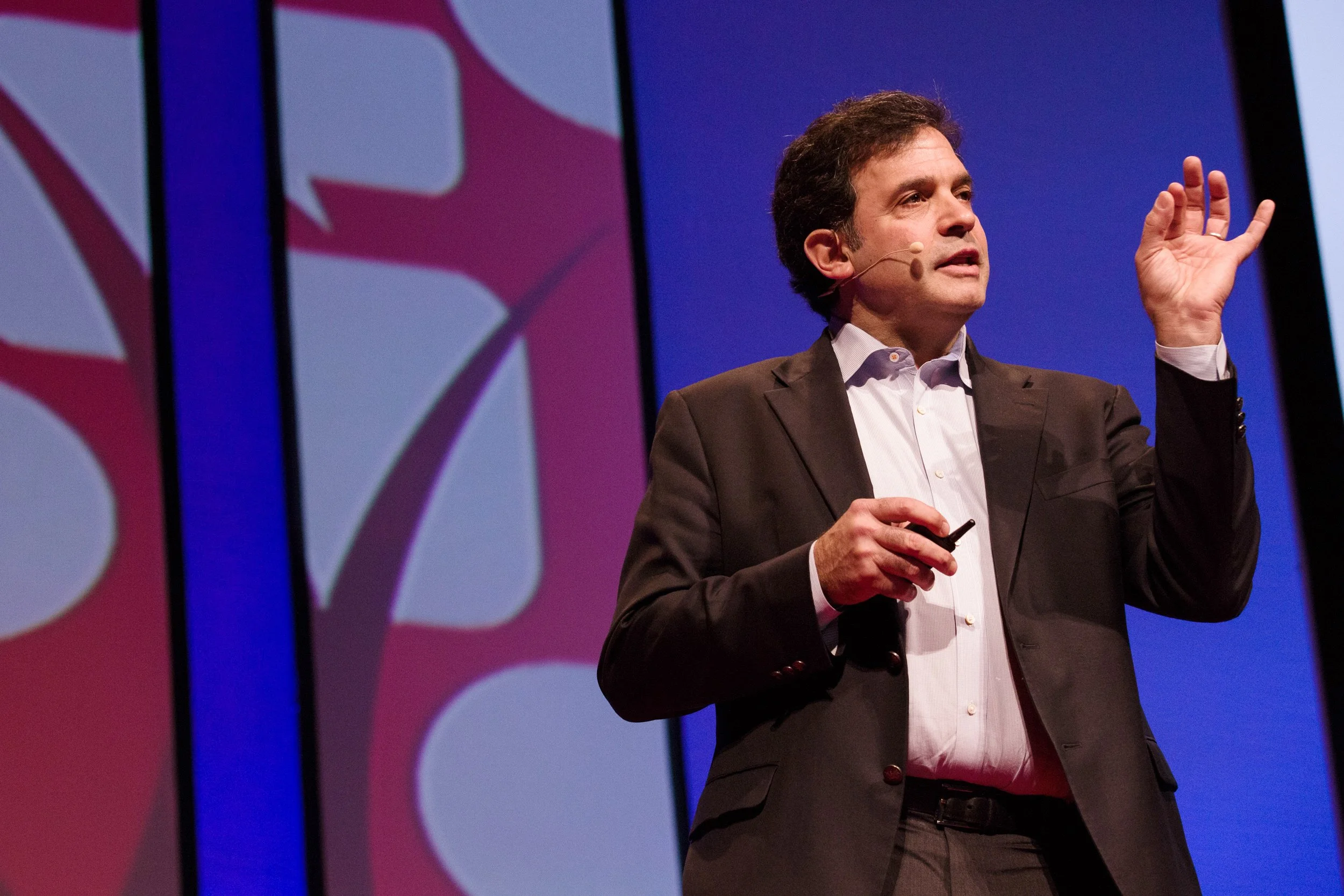 A man in a dark suit speaking on stage during TEDx talk in Boston.