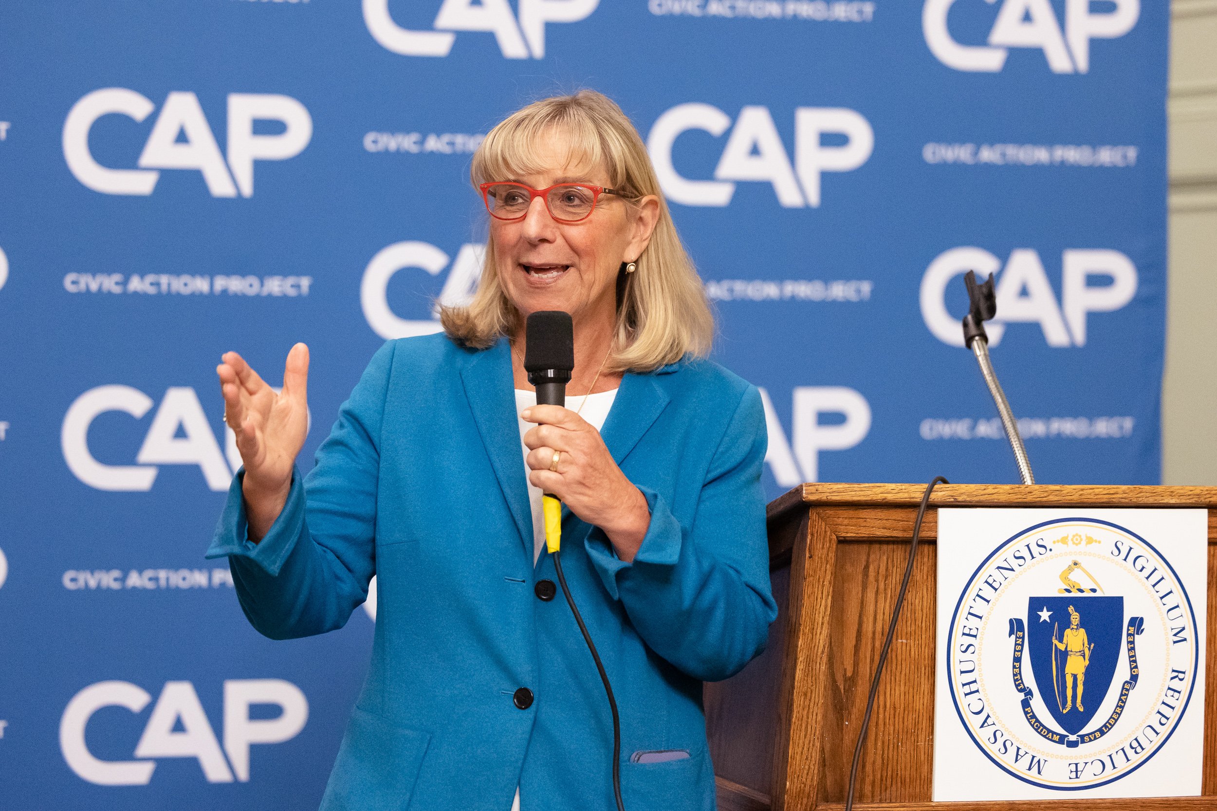 Karen Spilka speaking into a microphone at a podium with the Massachusetts seal at an even in Boston.