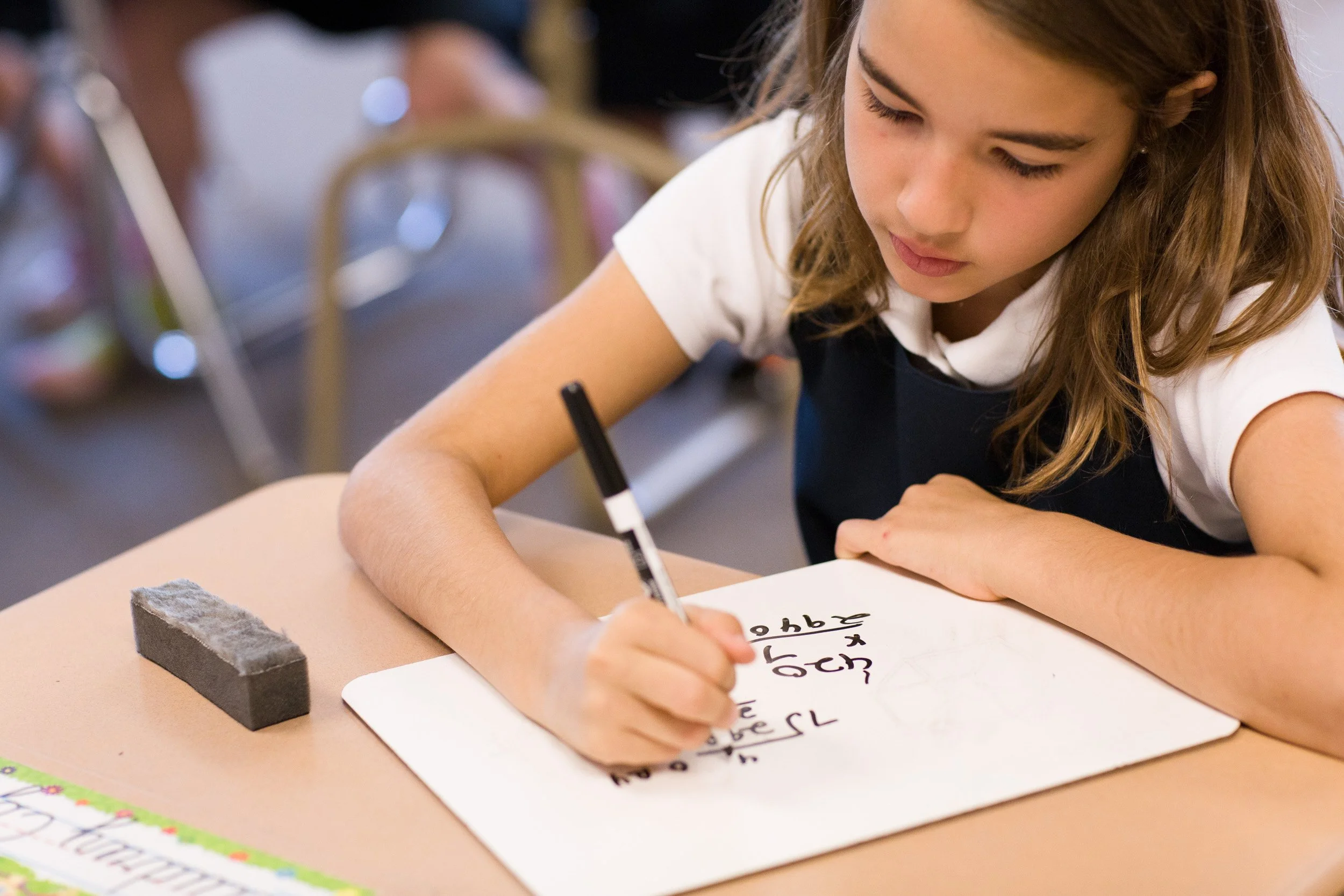 A young student writing on a white paper with a black marker at a Massachusetts private school.