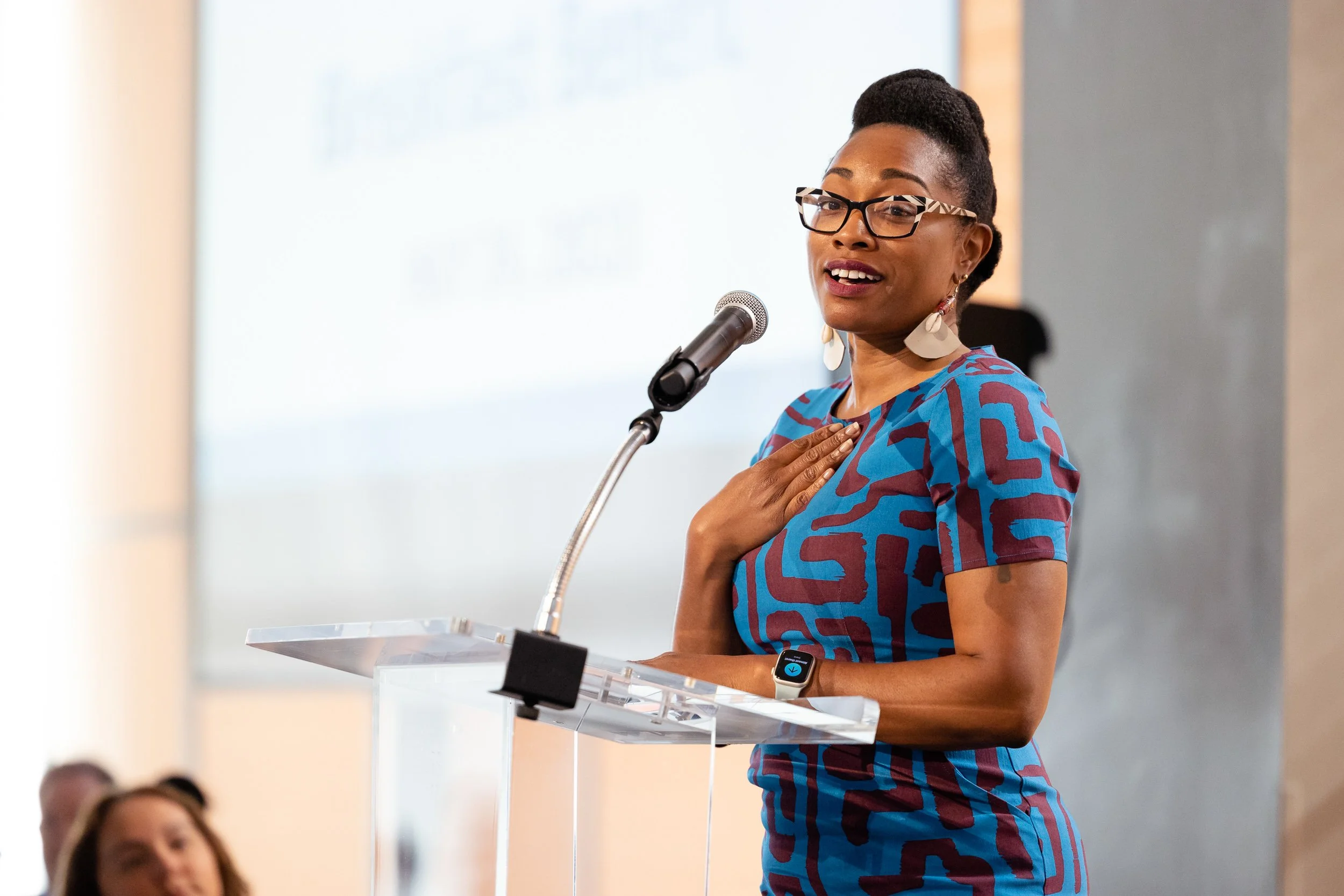 A woman standing at a podium and speaking into a microphone at a Compass Working Capital event in Boston.