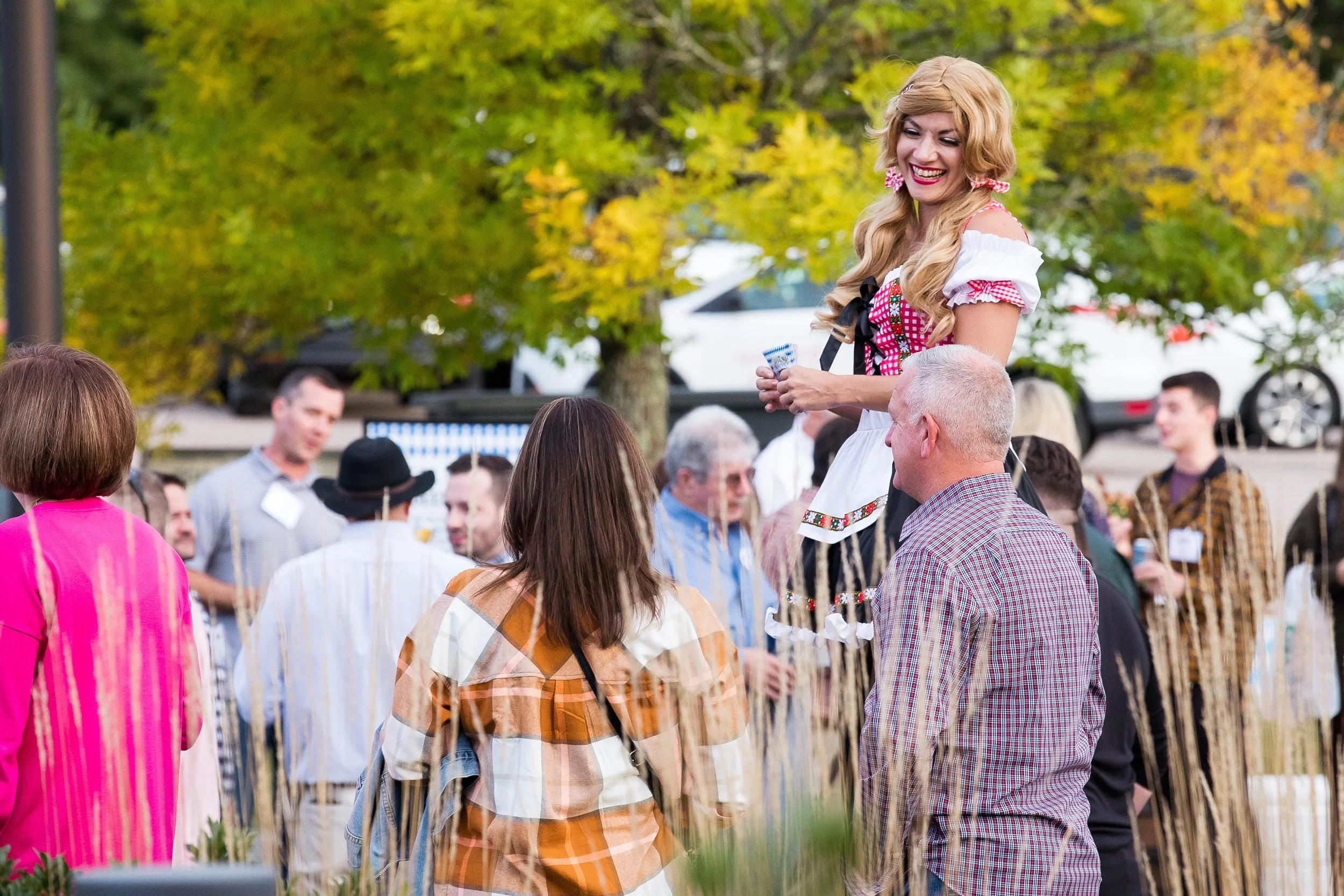 A woman dressed in traditional German attire speaking to a group of people outdoors  at an Oktoberfest event in Boston.