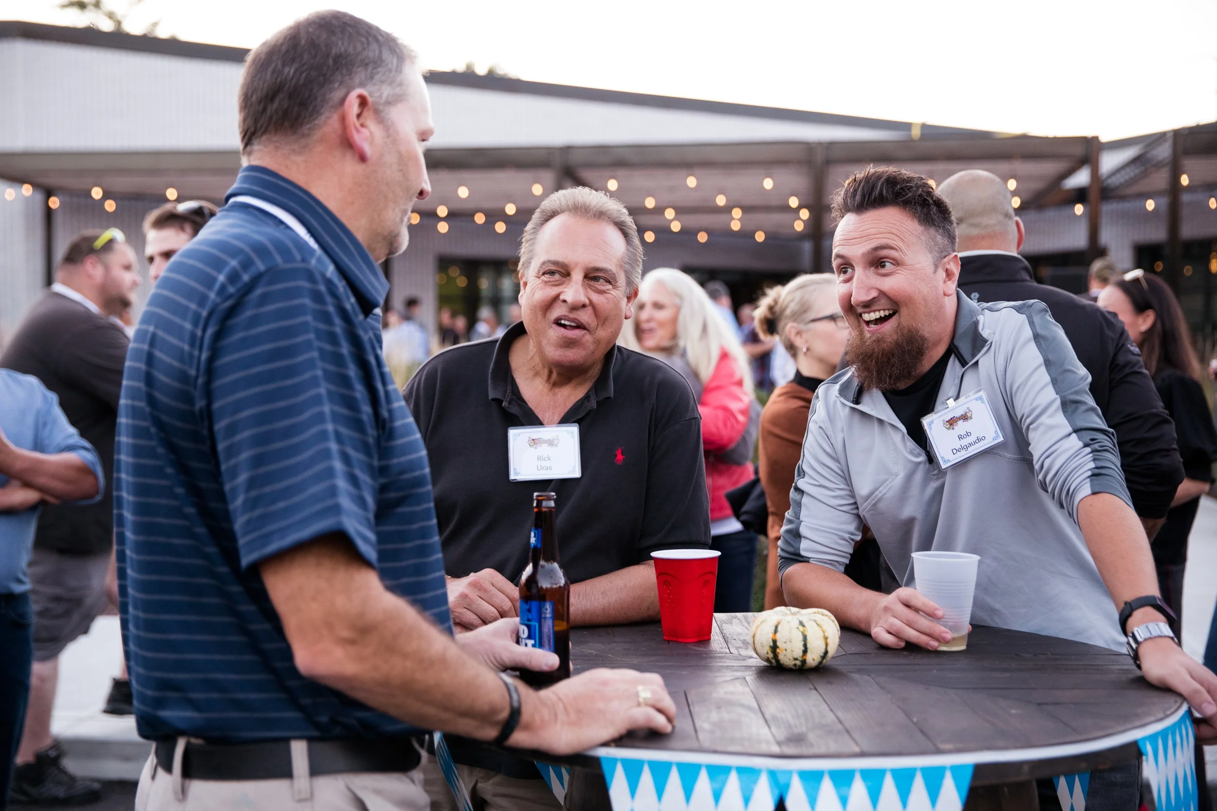 Three men talking together at an outdoor Oktoberfest celebration.