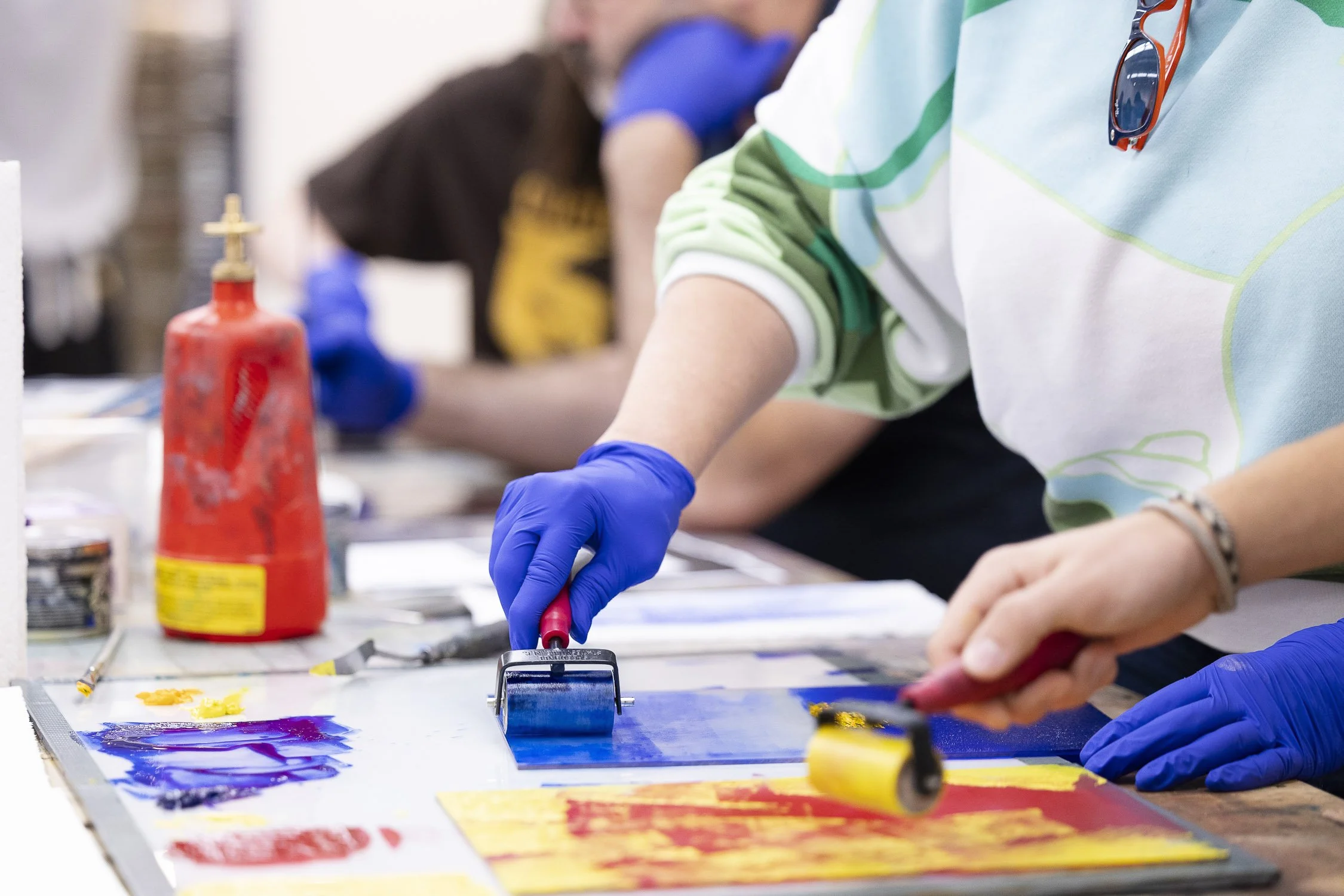 People working on vibrant painting projects with rollers and brushes in an art studio.