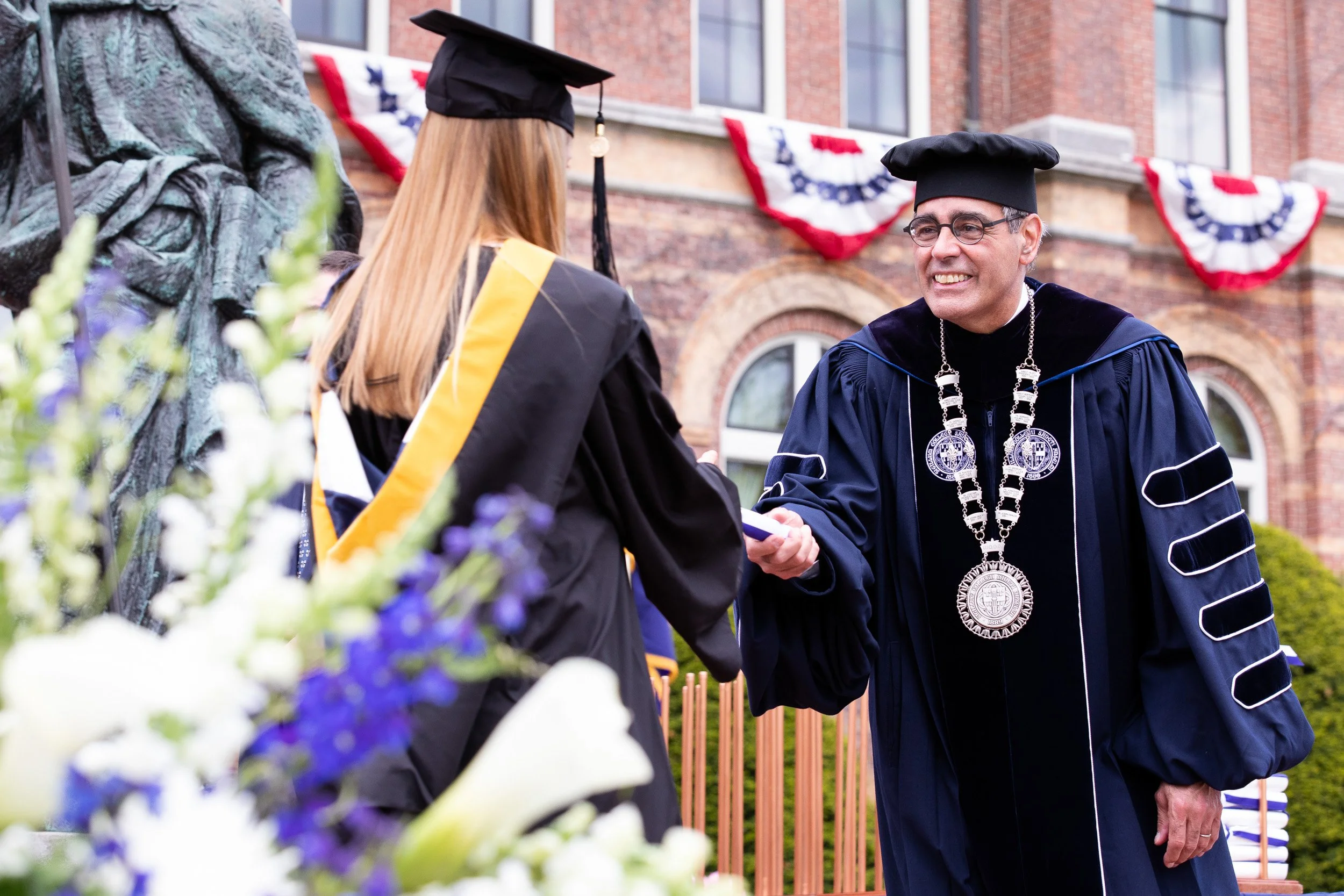A graduation ceremony with a faculty member in academic regalia shaking hands with a graduate in a cap and gown.