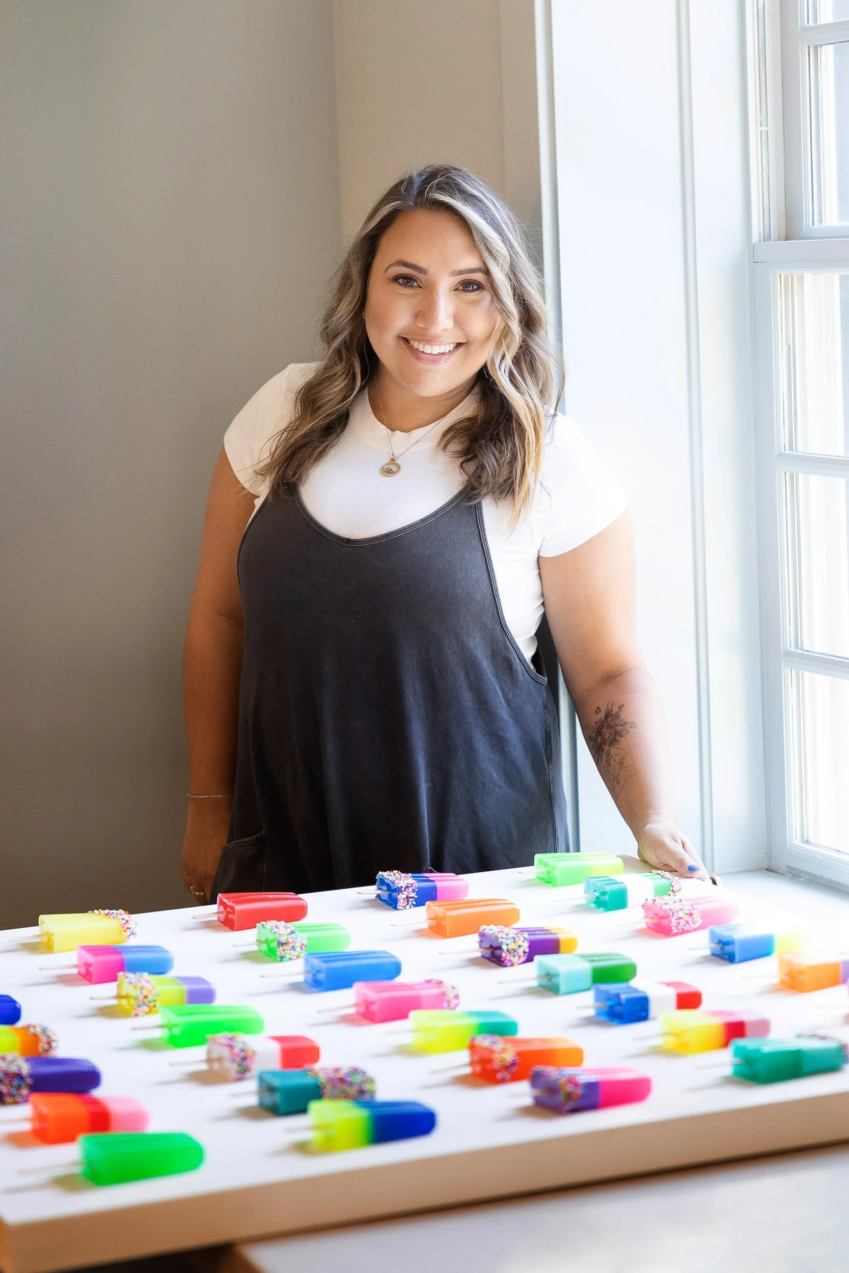A Newton artist standing behind artwork of colorful resin popsicles.