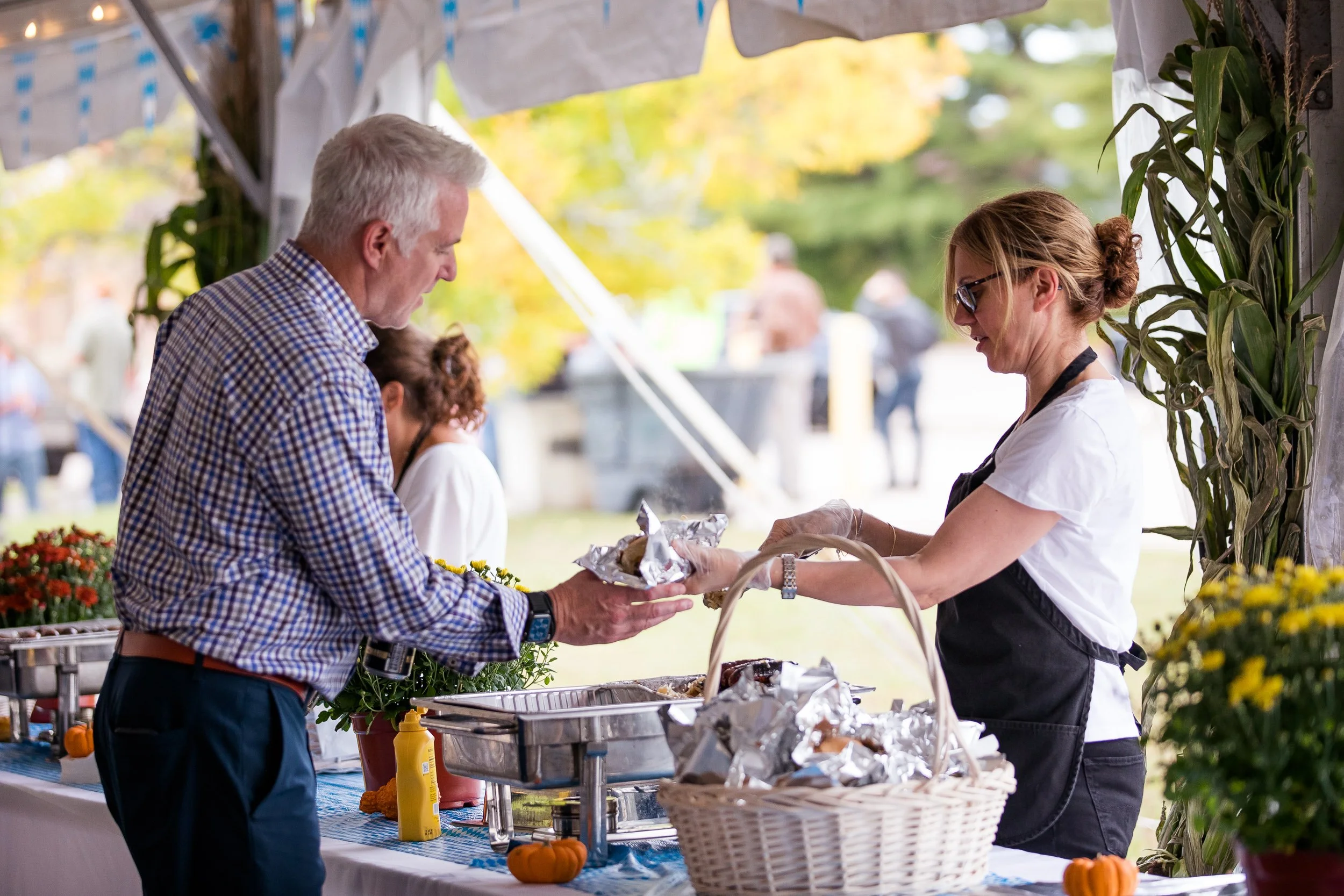 A man receives food from a woman serving at an outdoor food stand at an Oktoberfest event.