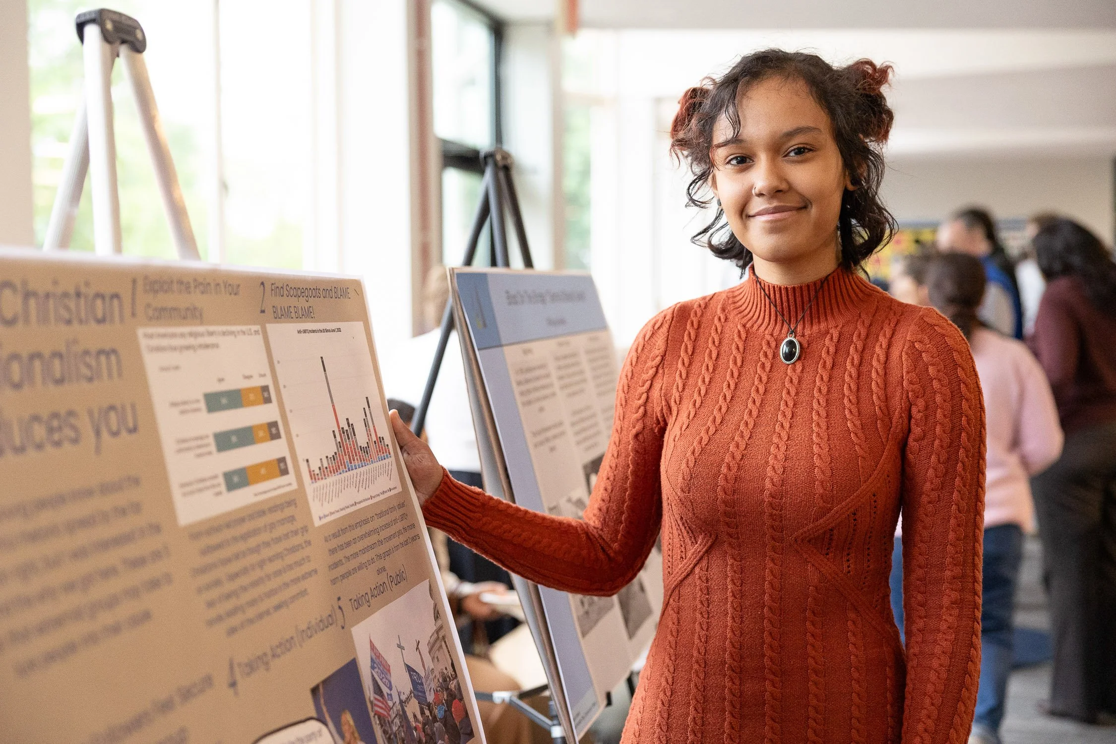 A student stands in front of a research poster at an indoor event at MassBay Community College.