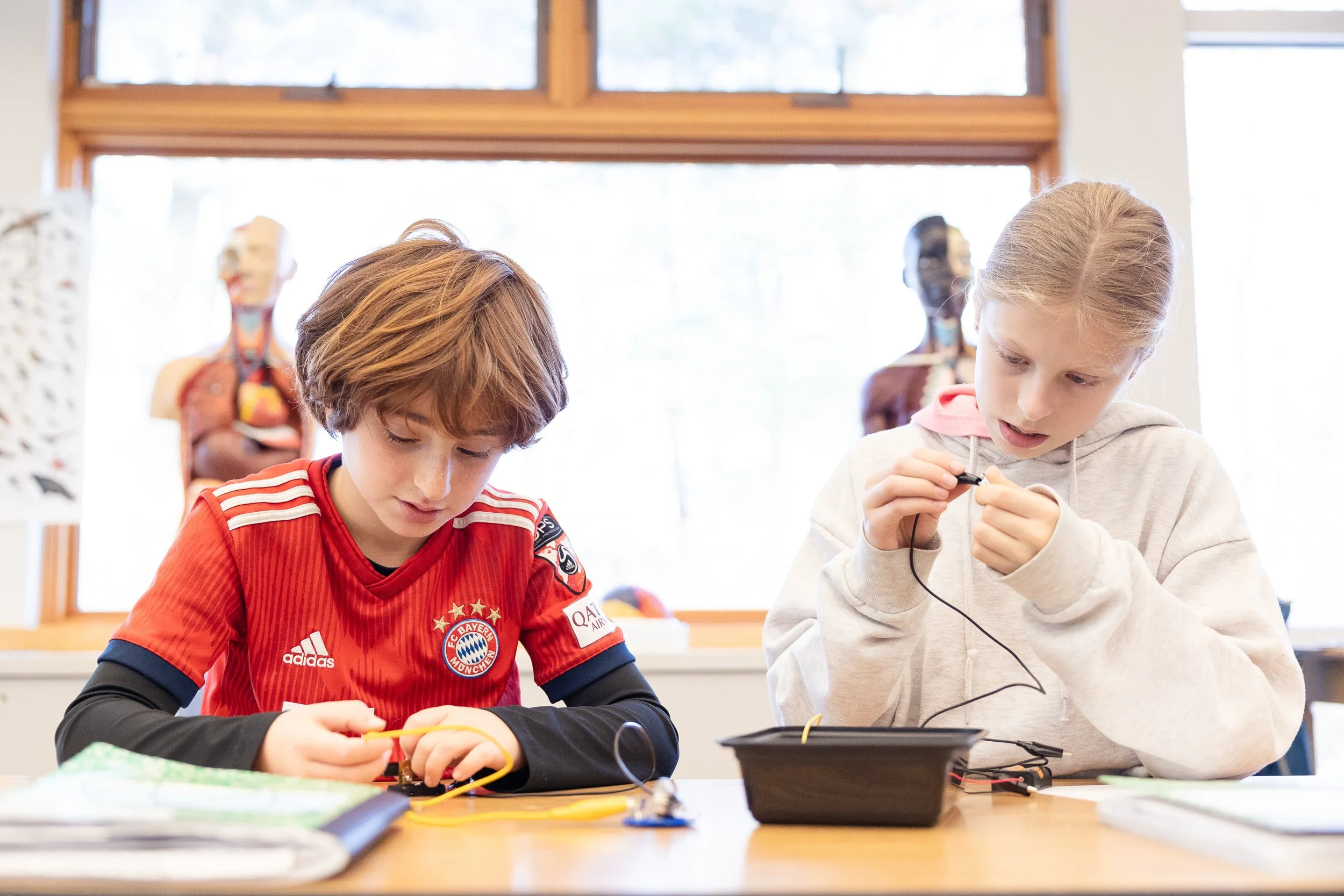Two children working on electronic projects at a classroom desk. 