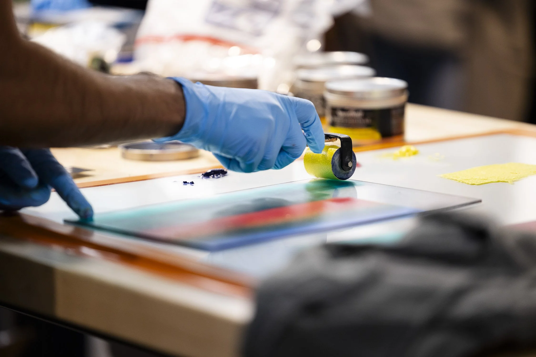 A person using a roller to press paint on a piece artwork on a tabletop. 