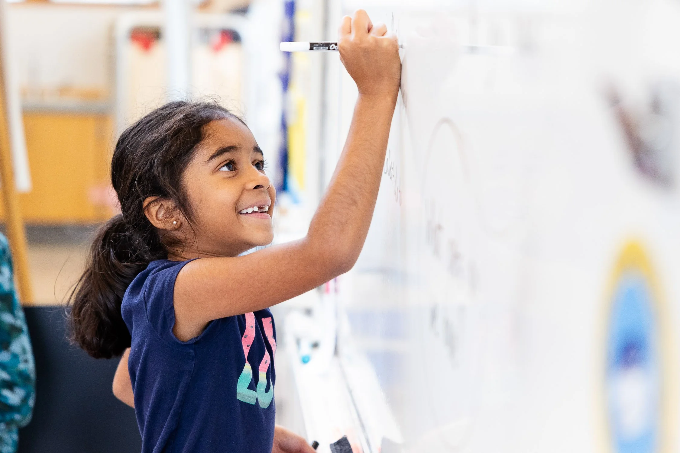 Elementary student writing on a whiteboard in a classroom.