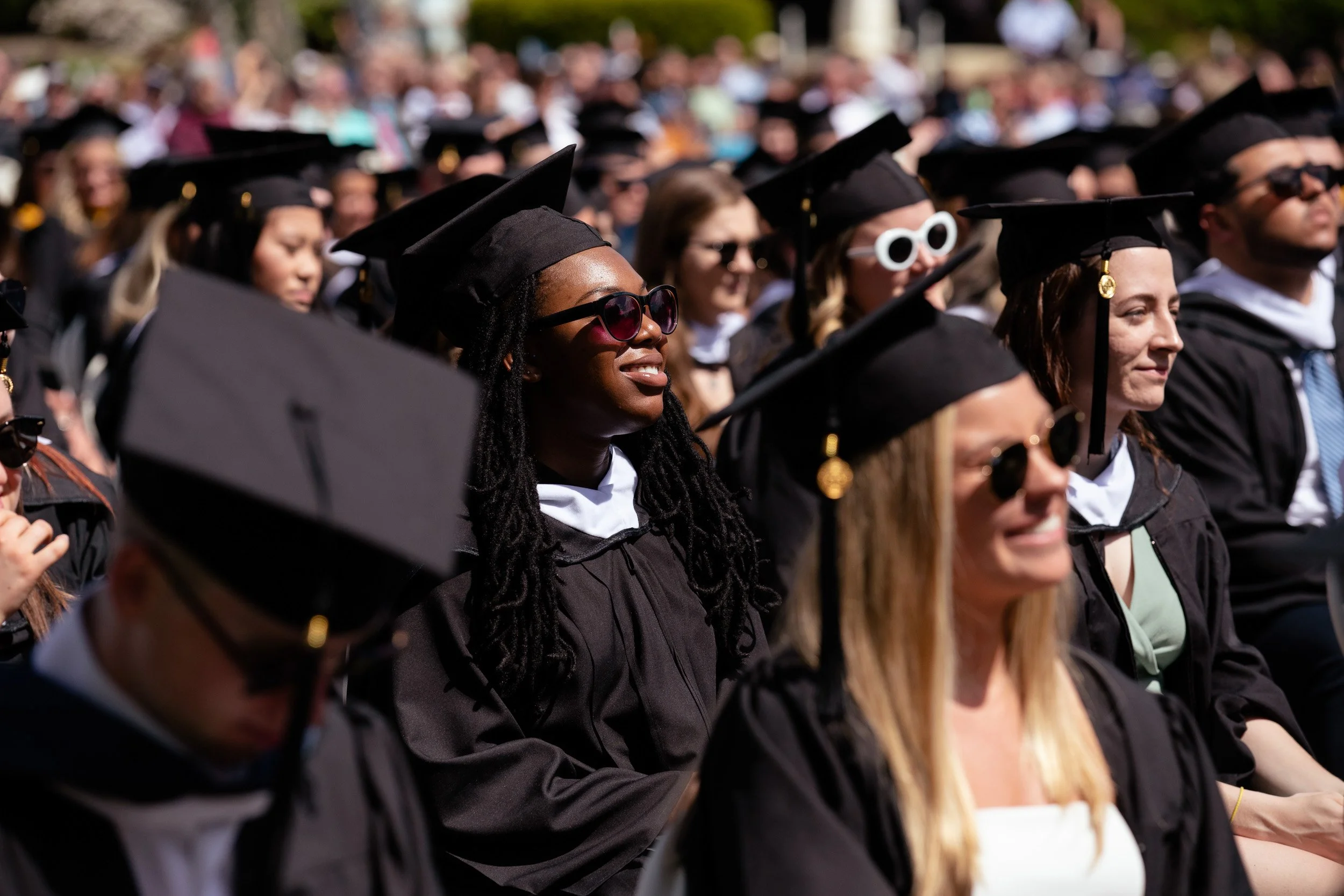 A large group of graduation students in caps and gowns sitting outdoors during a commencement ceremony in New Hampshire.