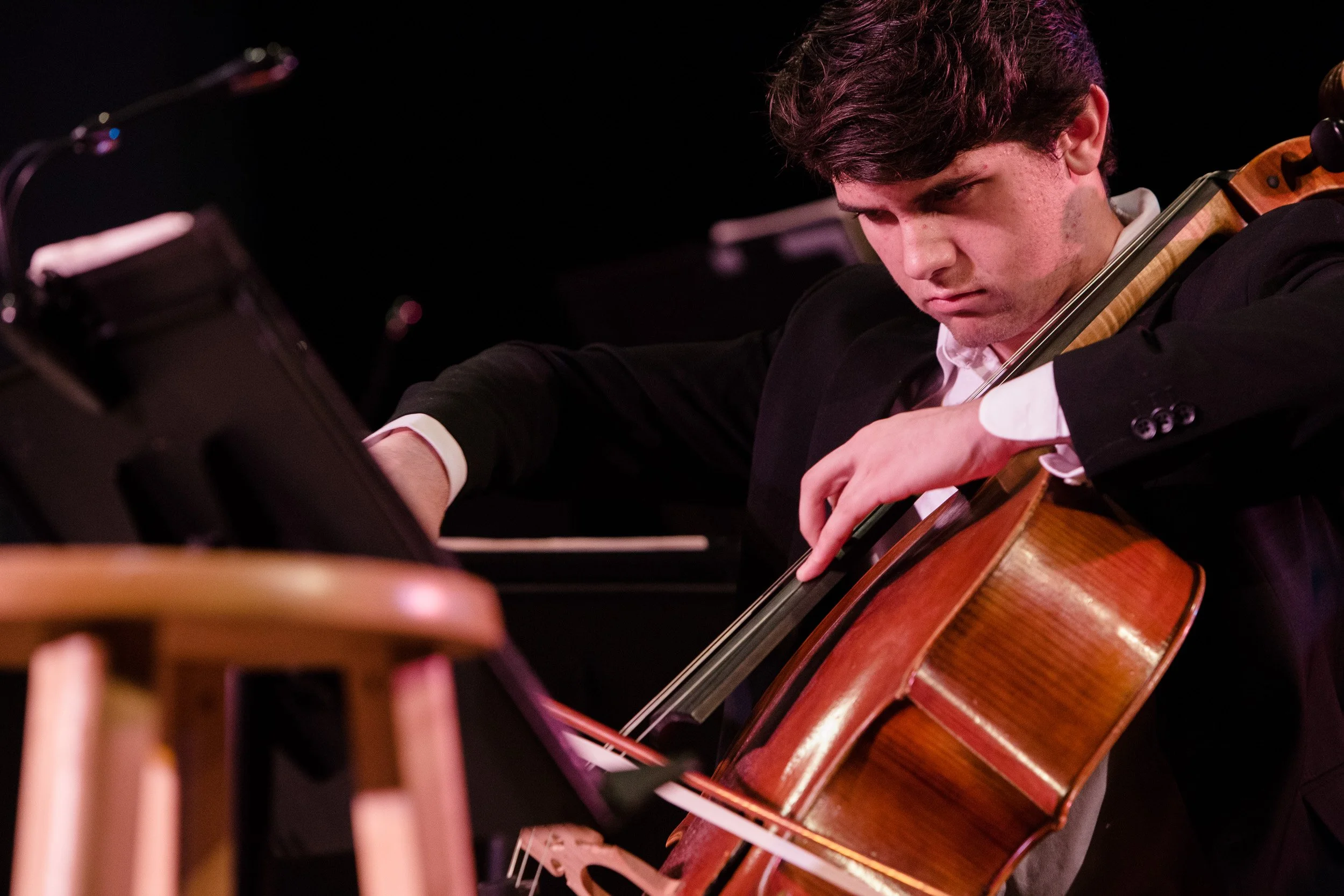 Young man in formal attire playing a cello during a performance.