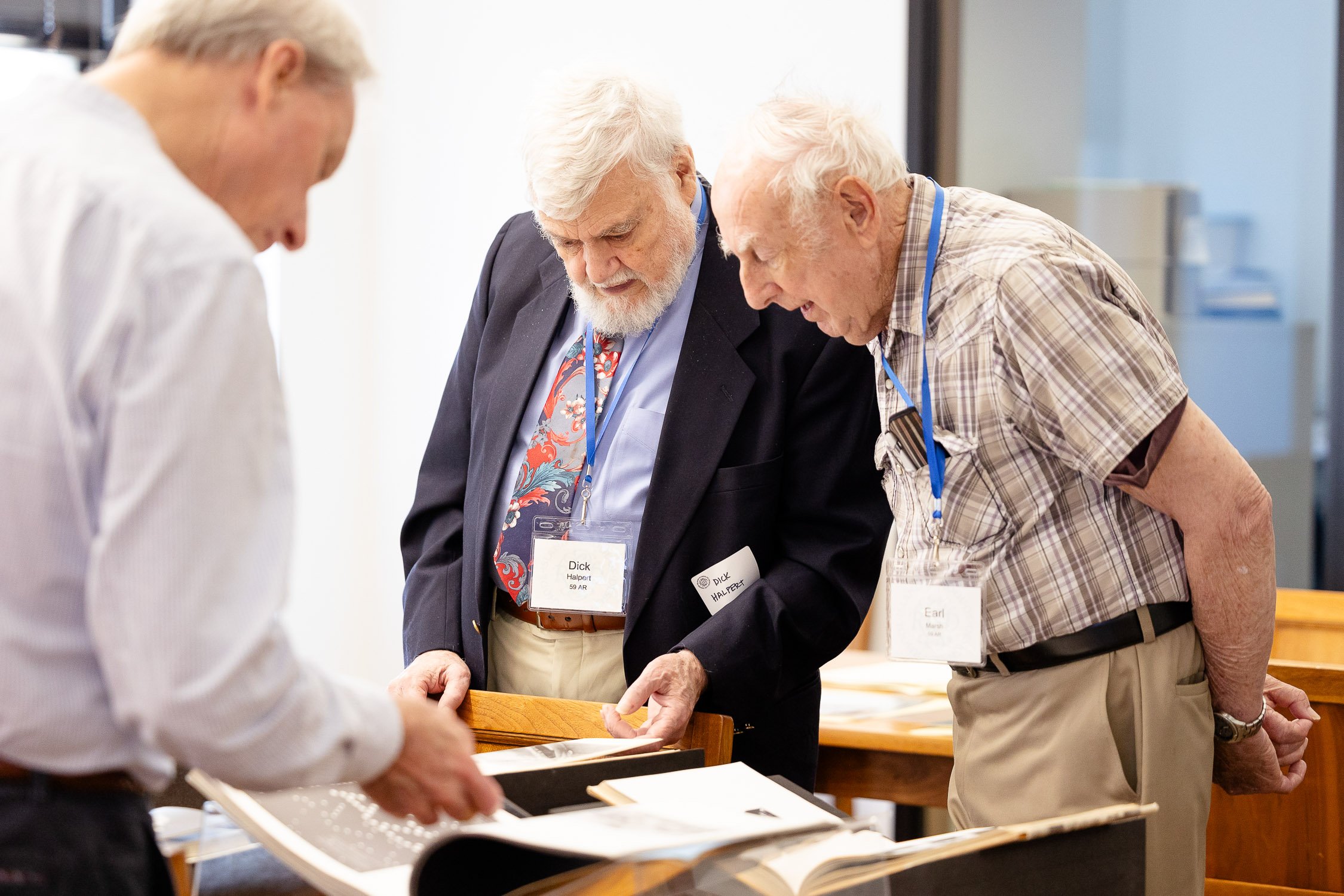 Three elderly men looking at photo albums on a table during college reunion.